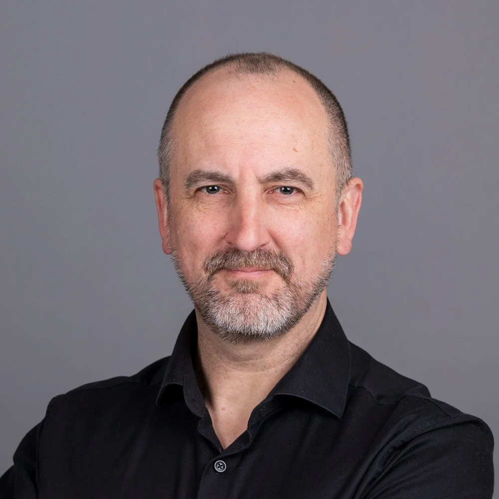 Staff headshot from an on-site team shoot in Waterloo, London. Man in a black shirt on a grey backdrop