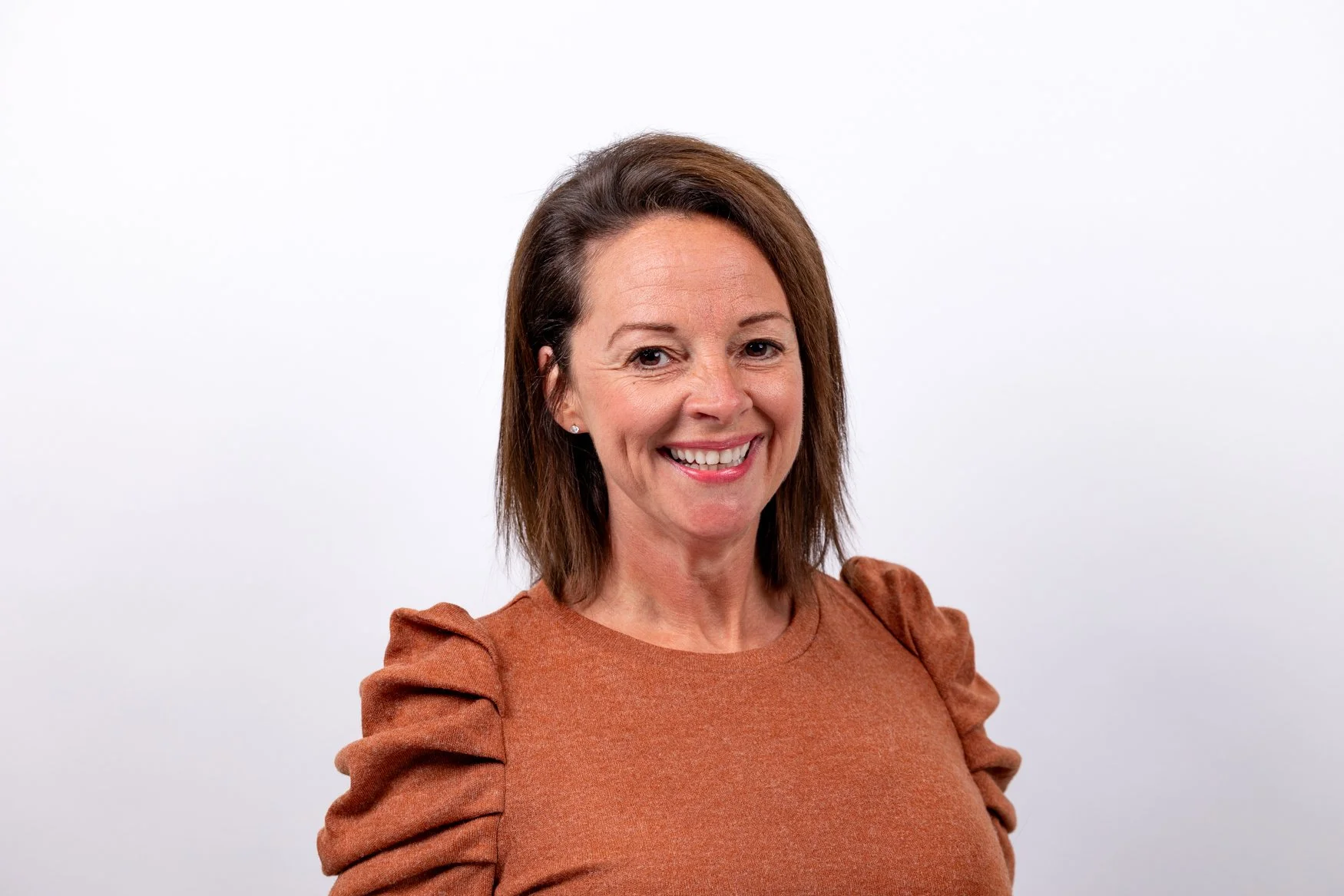 Smiling woman in a rust-coloured top on a soft white background, a LinkedIn headshot for a new job in London