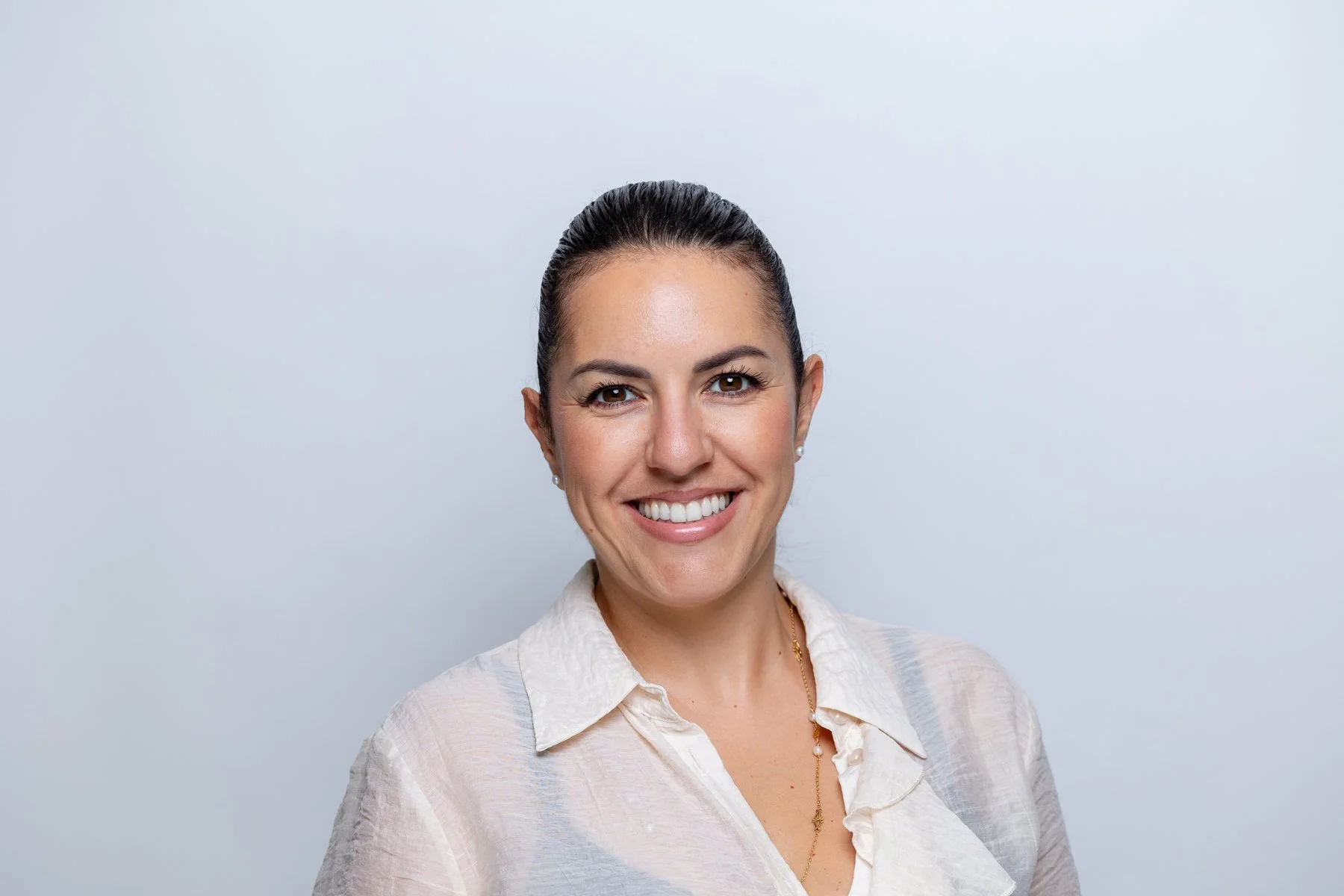 Studio headshot of a smiling woman in a cream linen shirt against a light grey background, by Shot By Andrew