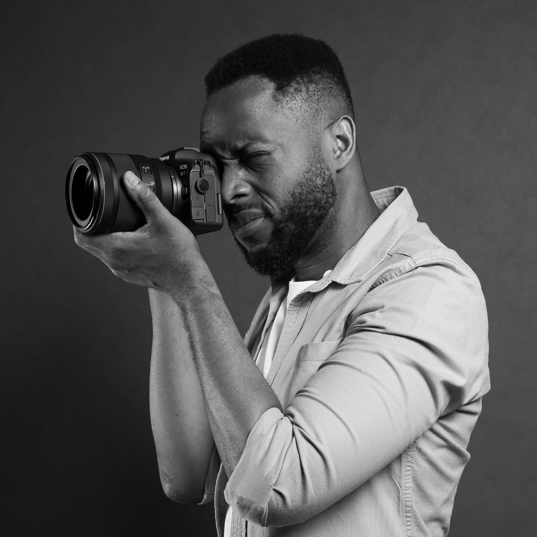 London headshot photographer holding a camera to his eye during a shoot, in black and white