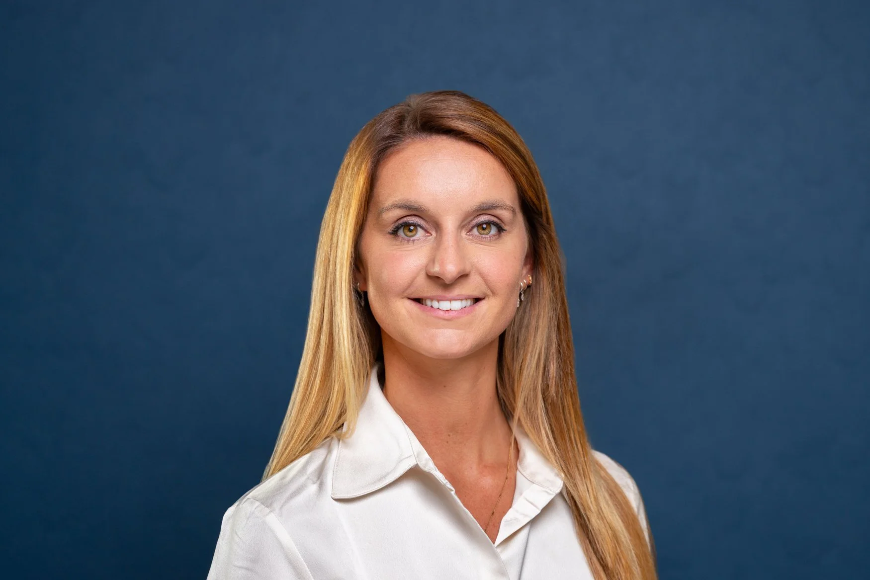 Smiling blonde woman in a white shirt on a navy background, a LinkedIn headshot by a London headshot photographer