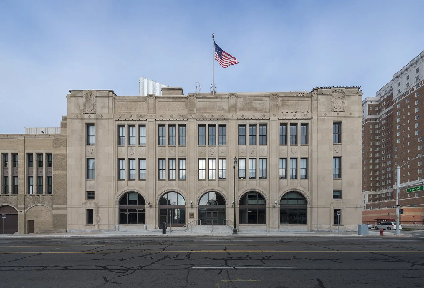 Facade of a historic government or municipal building with an American flag on top, large arched windows, and a street view in an urban setting.