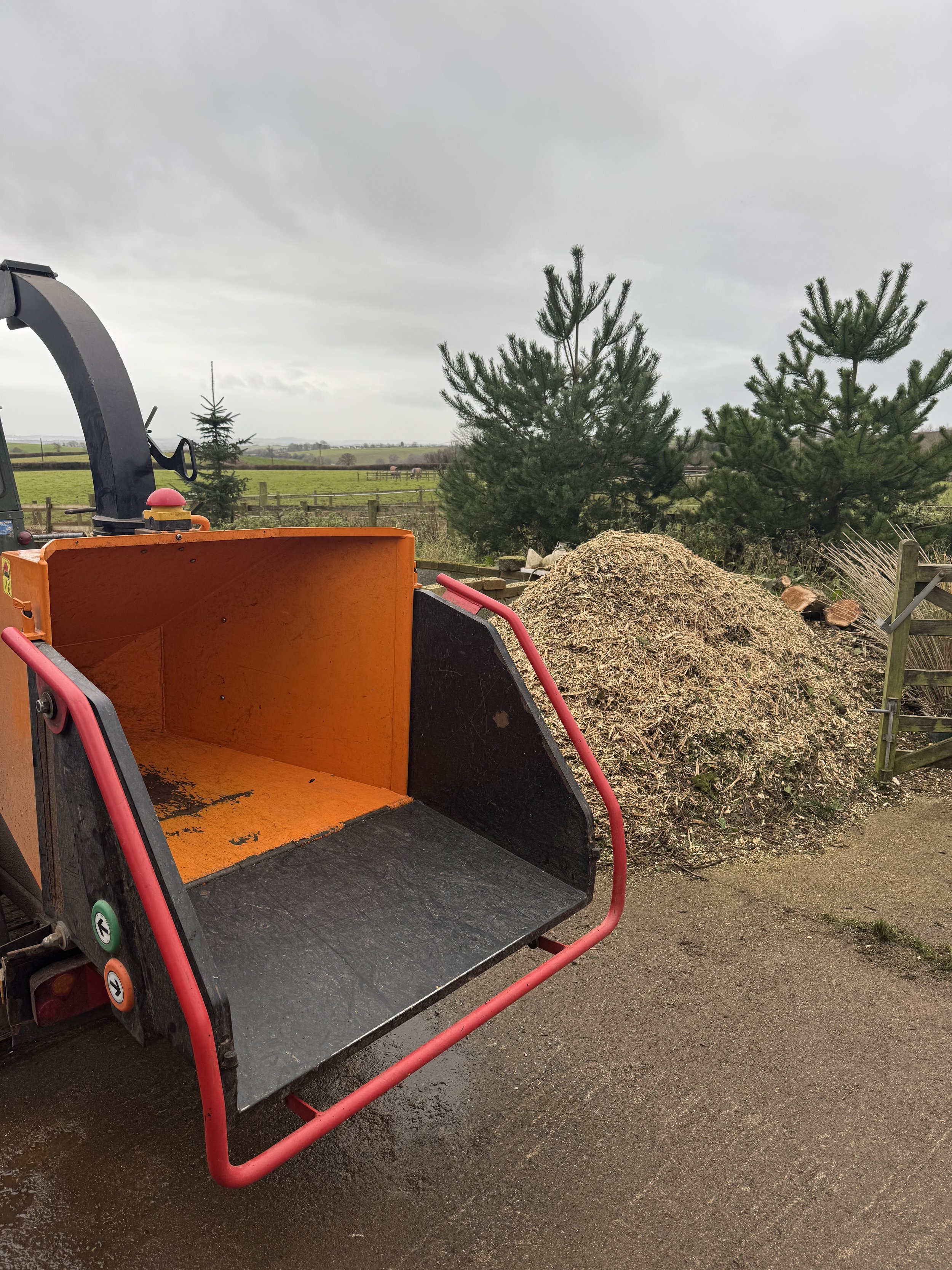 A wood chipper with a pile of wood chips and logs