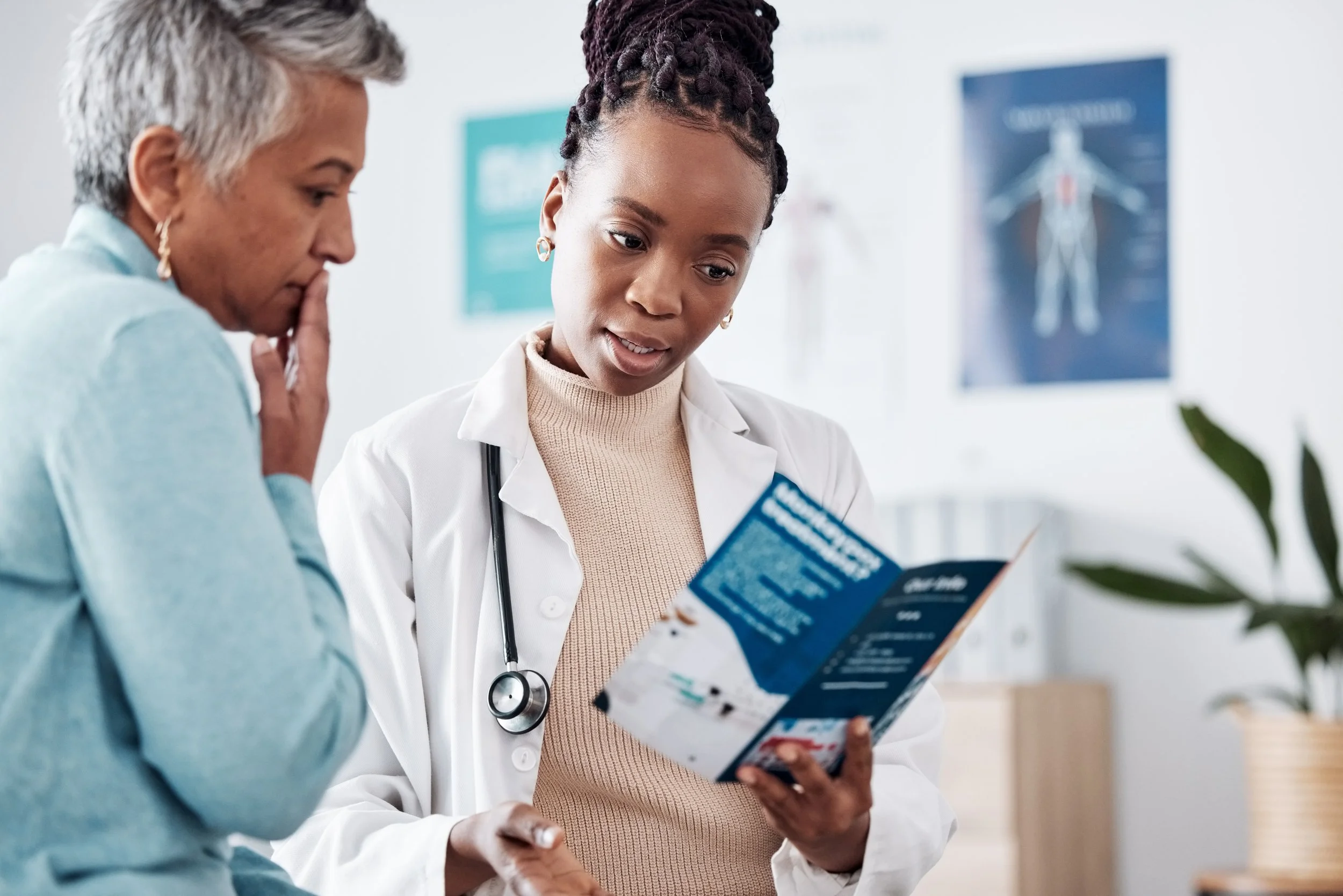 A doctor talking to a woman while both looking at a brochure.