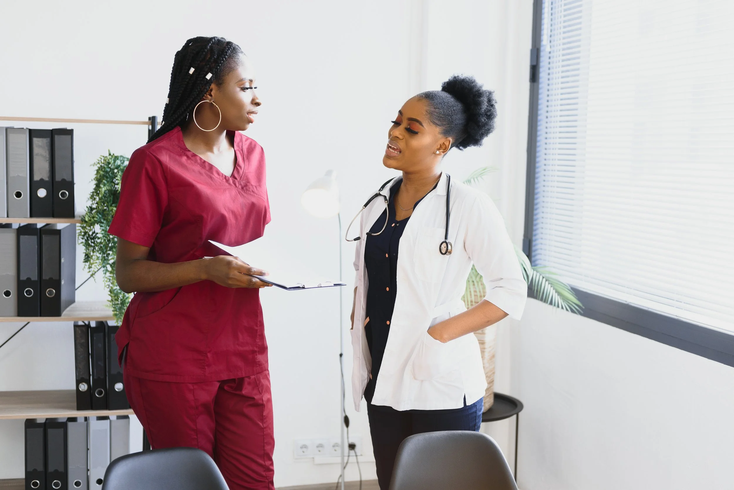 Two Black health professional women are standing and talking.