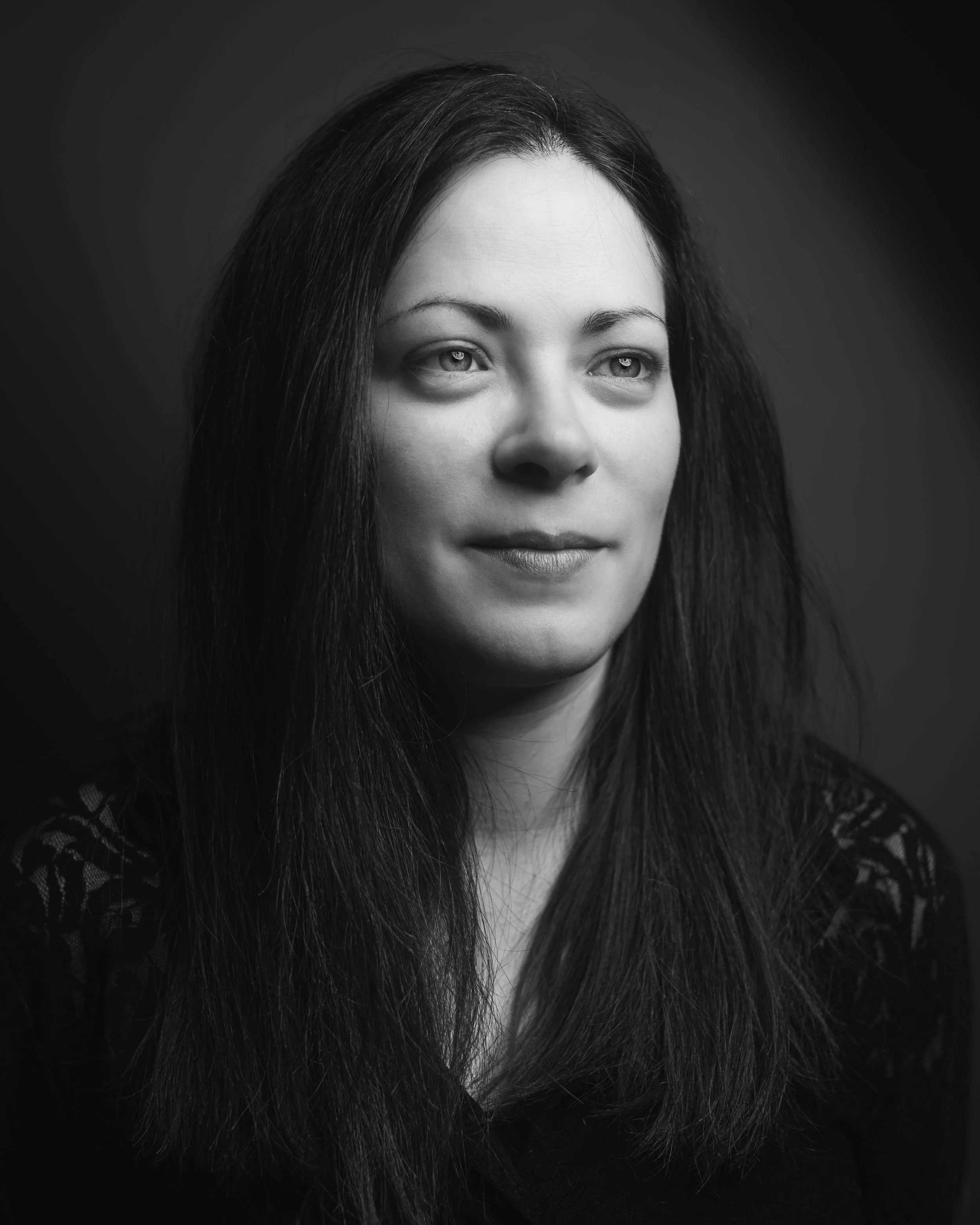 Un portrait en noir et blanc d'une femme avec de longs cheveux foncés, regardant légèrement à droite, portant un vêtement à motif sur l'épaule.