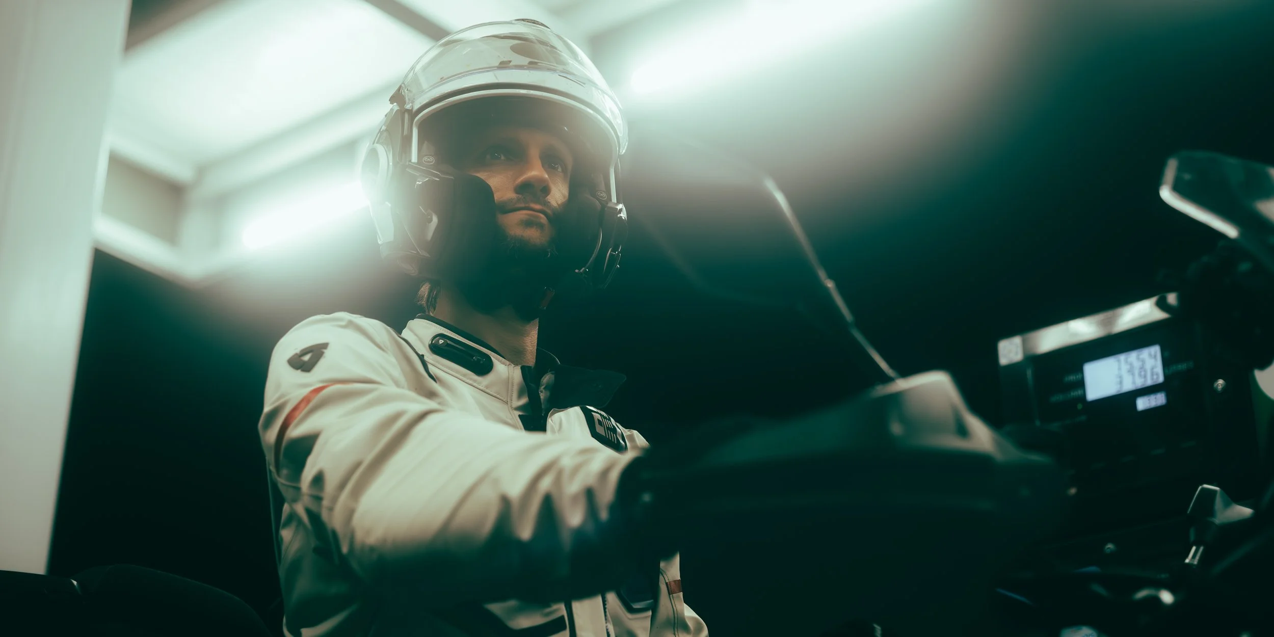 Pilote de course en tenue blanche et casque dans une voiture de course, vue en contre-plongée avec lumière de fond.
