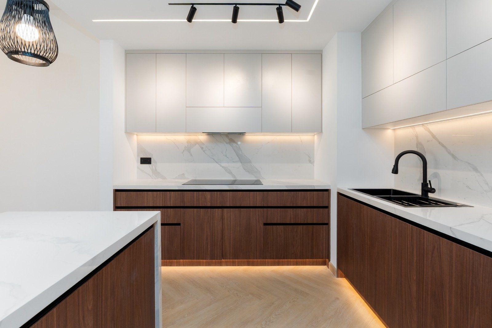 Modern kitchen with white upper cabinets, dark wood lower cabinets, marble backsplash, and a black sink and faucet.