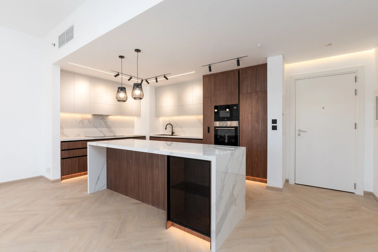 Modern kitchen with white and wooden cabinetry, marble countertops, an island with marble and wood panels, a black oven, pendant lights, and track lighting.
