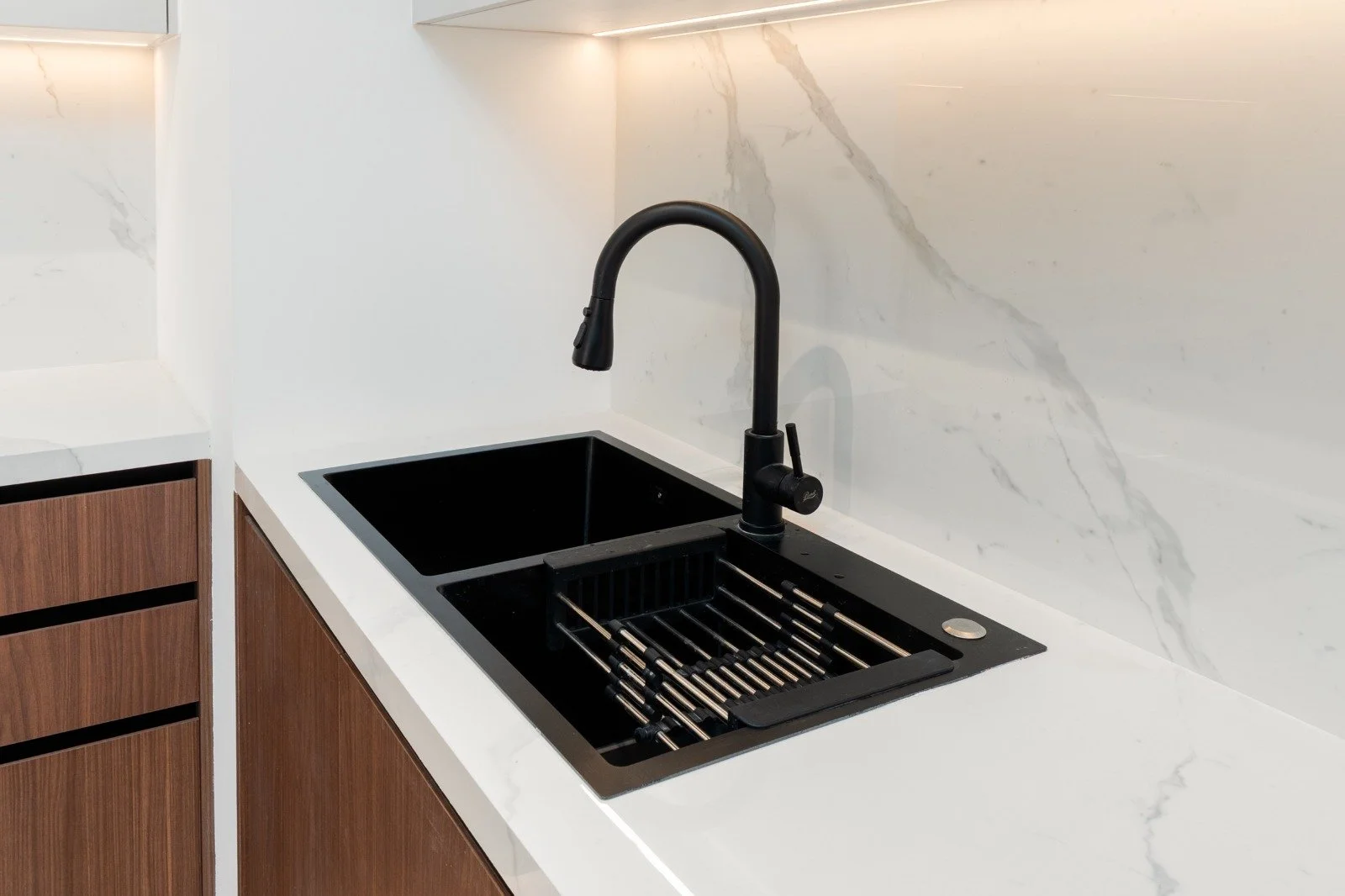 Modern kitchen with a black sink and chrome rack, white marble backsplash, and wooden cabinet underneath.