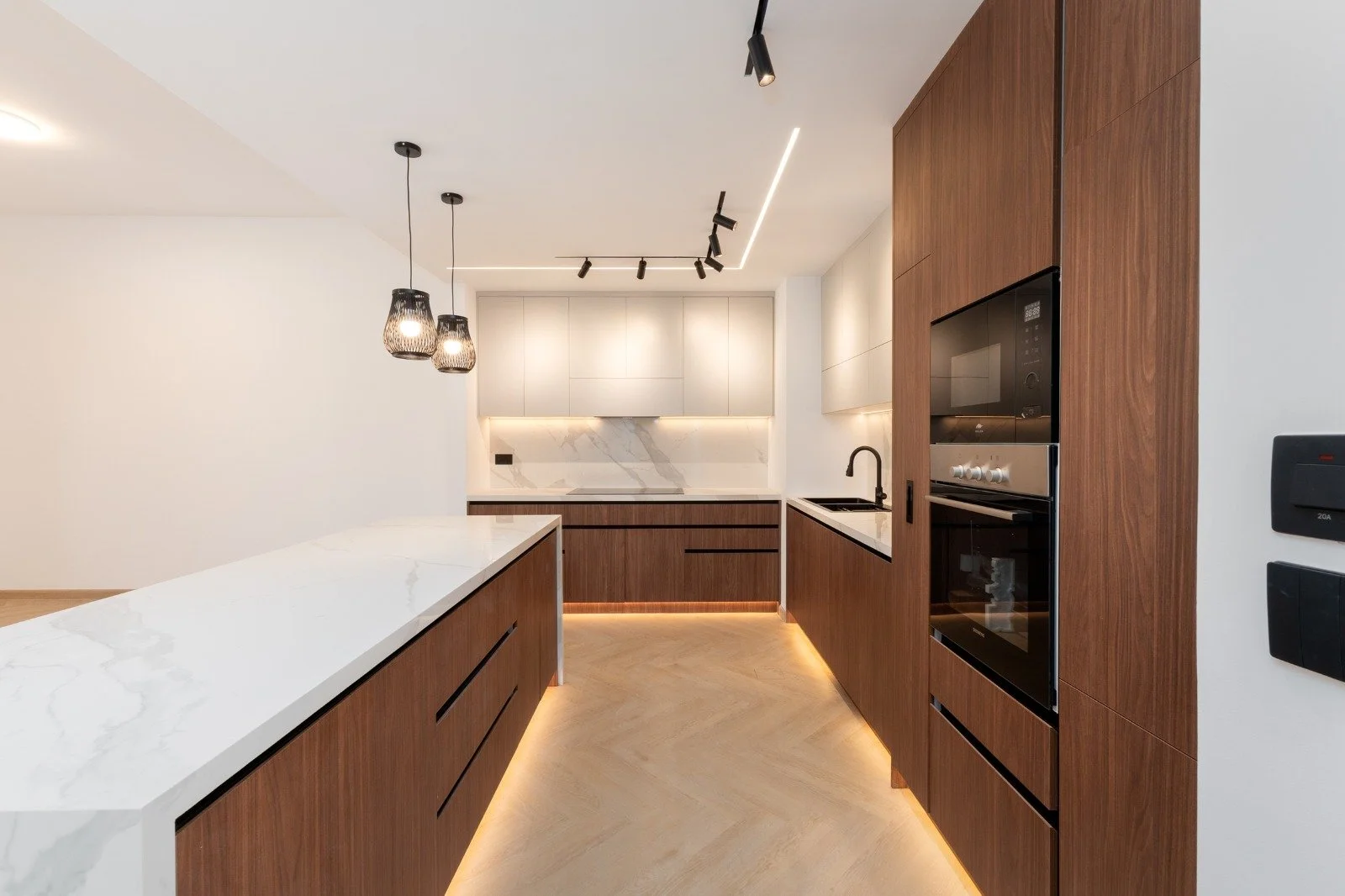 Modern kitchen with wooden cabinets, white marble countertops, black fixtures, and warm lighting to create a sleek, minimalist space.