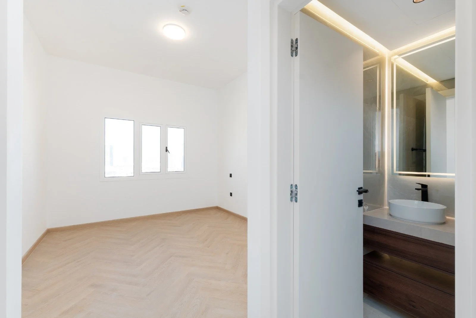 Empty room with three windows, pendant ceiling light, and a partially visible bathroom with a sink and a mirror.