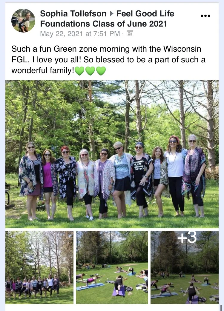 Group of women posing outdoors in a park setting with yoga mats on the grass, surrounded by trees and greenery, during an event.