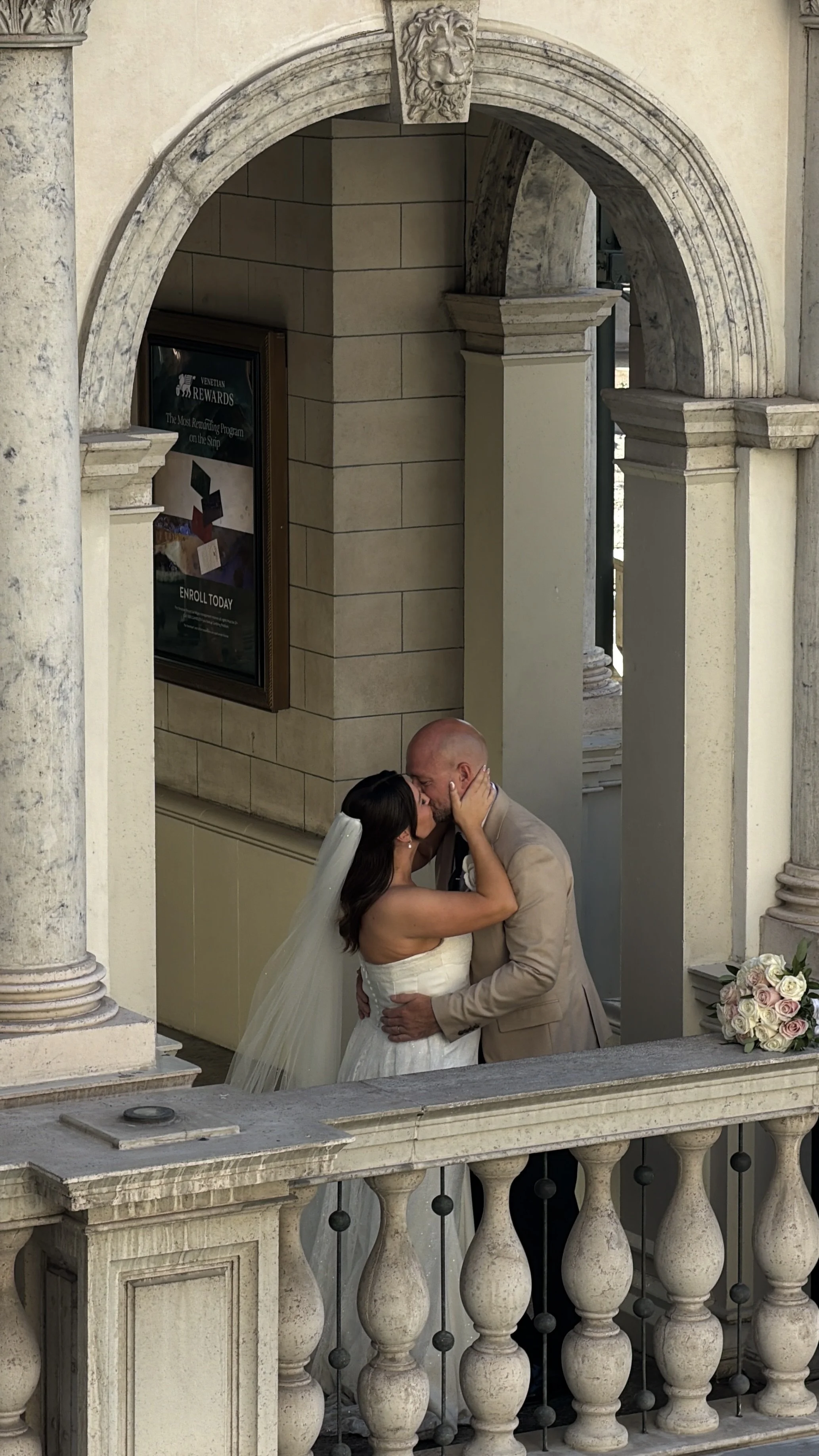 A bride and groom sharing a kiss on a balcony with ornate stone columns and decorative architecture.