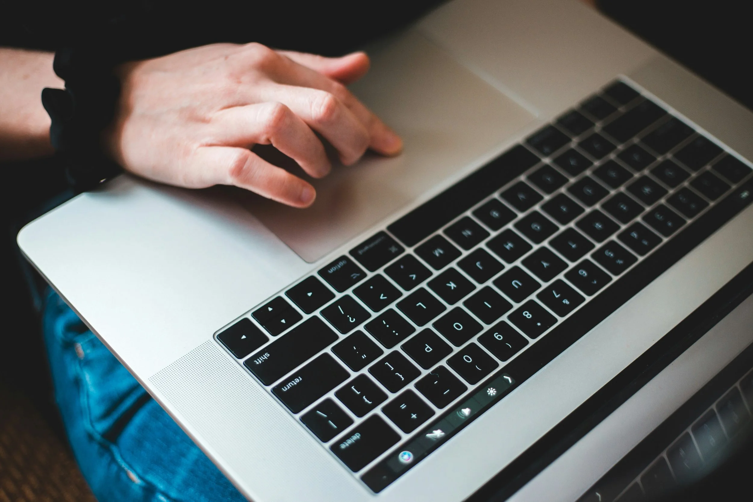 Close-up of a person's hand on a laptop keyboard, with jeans visible in the background.