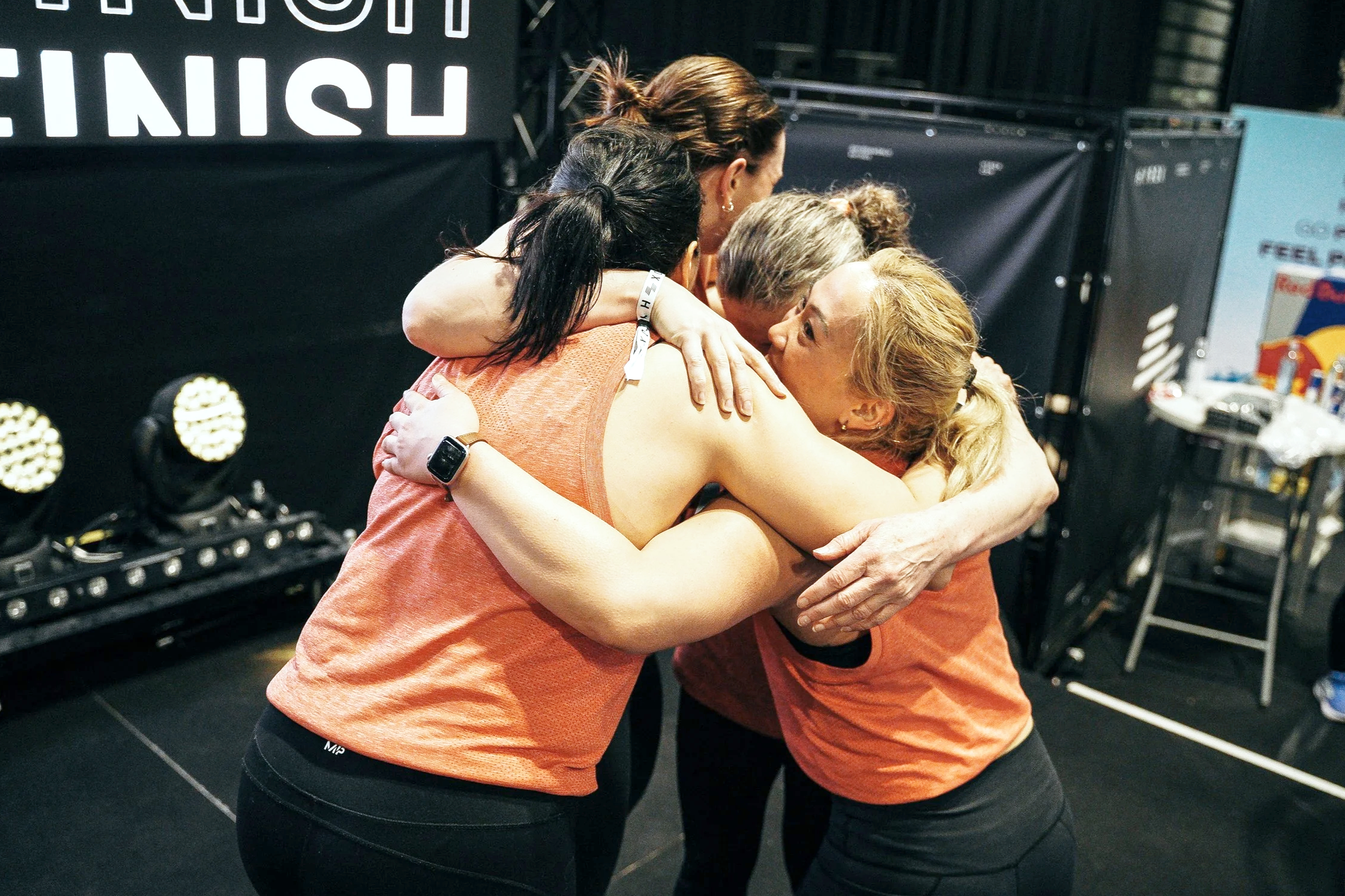Group of women hugging and celebrating after an event in a gym or sports arena.