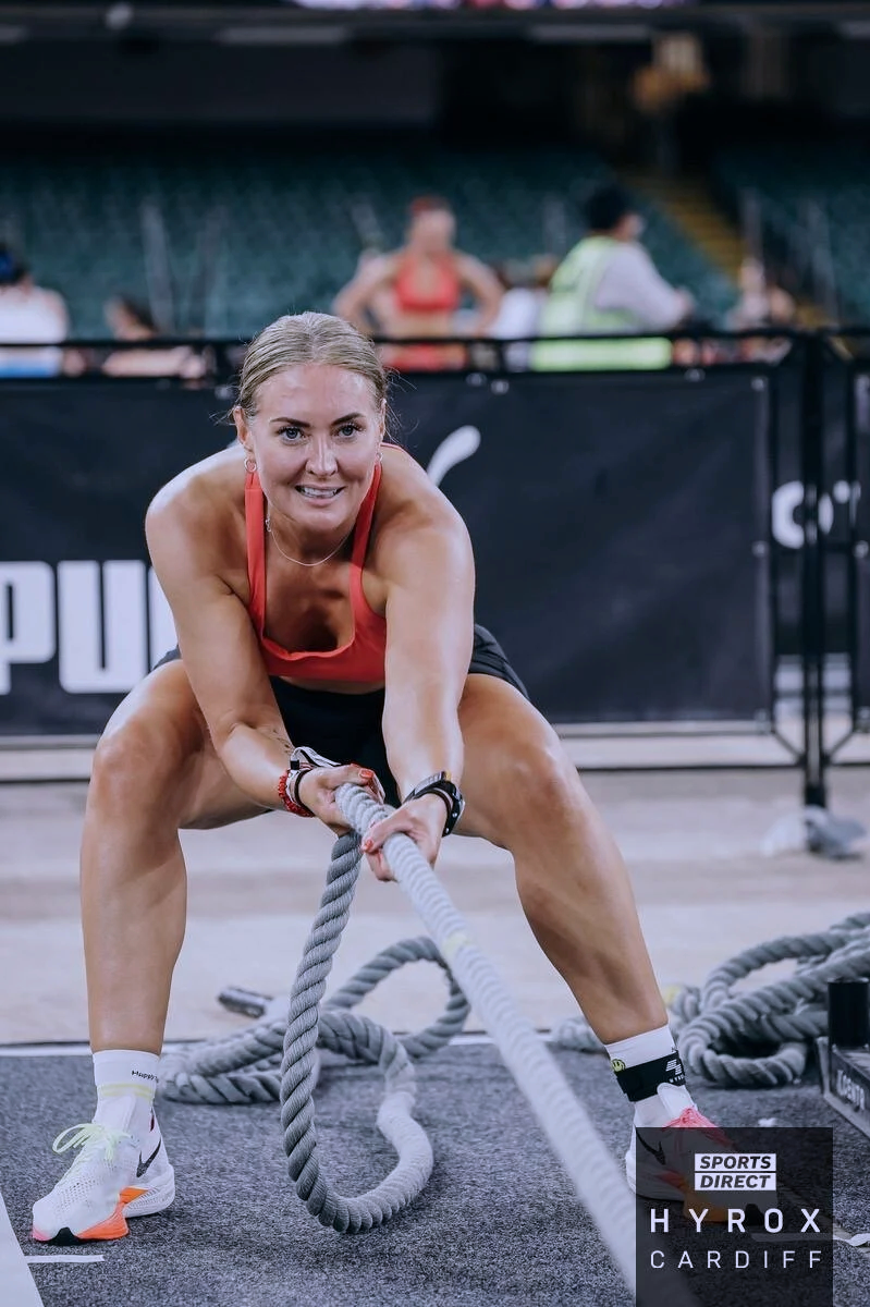 Female athlete in workout gear pulling a battle rope during intense exercise at a sports event.
