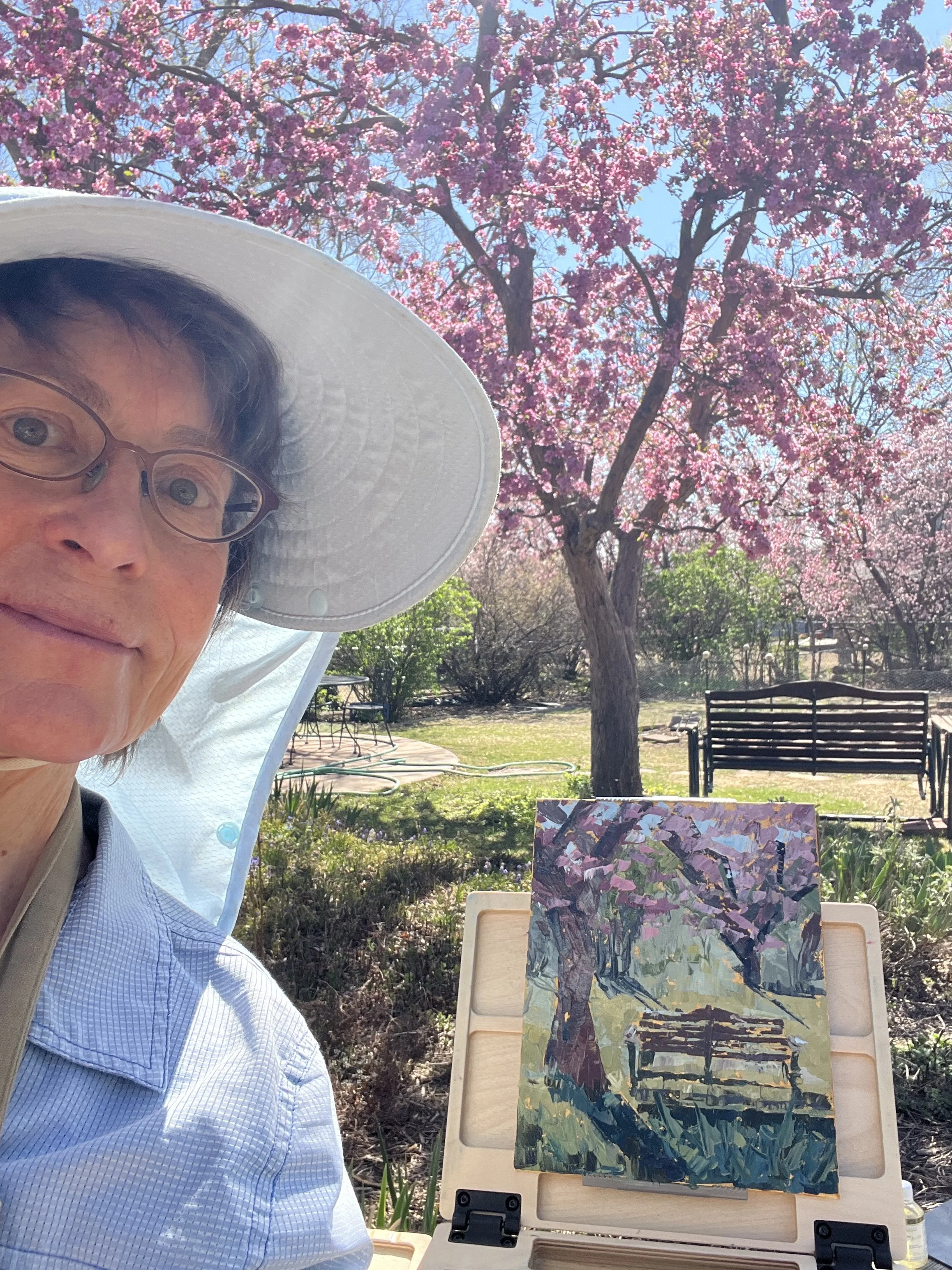 Lisa in her backyard with the painting and the pink flowering tree