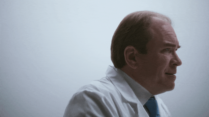 Side profile of a man in a white shirt and blue tie against a plain light background.
