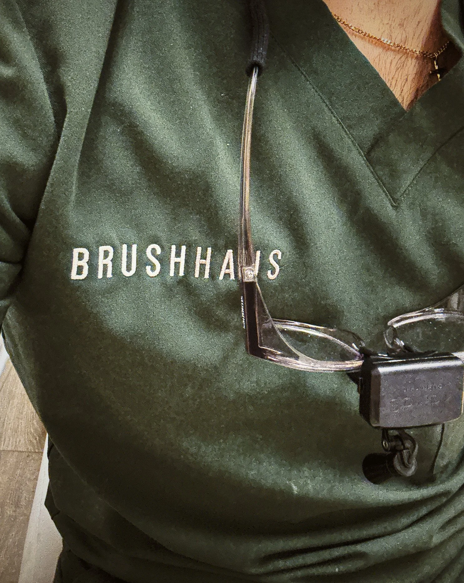 Close-up of a person wearing a green shirt that says 'BrushHaus', with a stethoscope and safety glasses hanging around their neck.