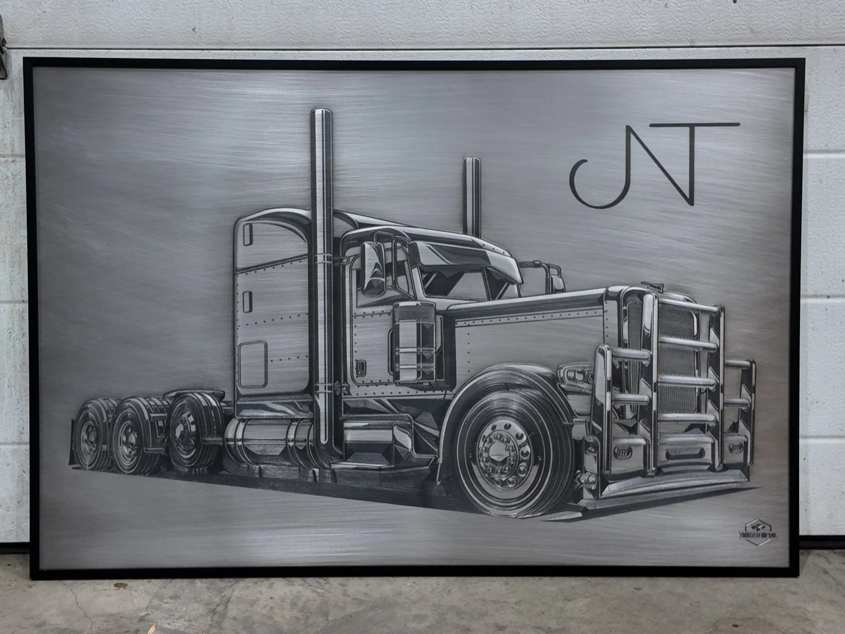 A black and white metallic artwork of a semi-truck, with detailed shading and reflections, framed and mounted on a wall.