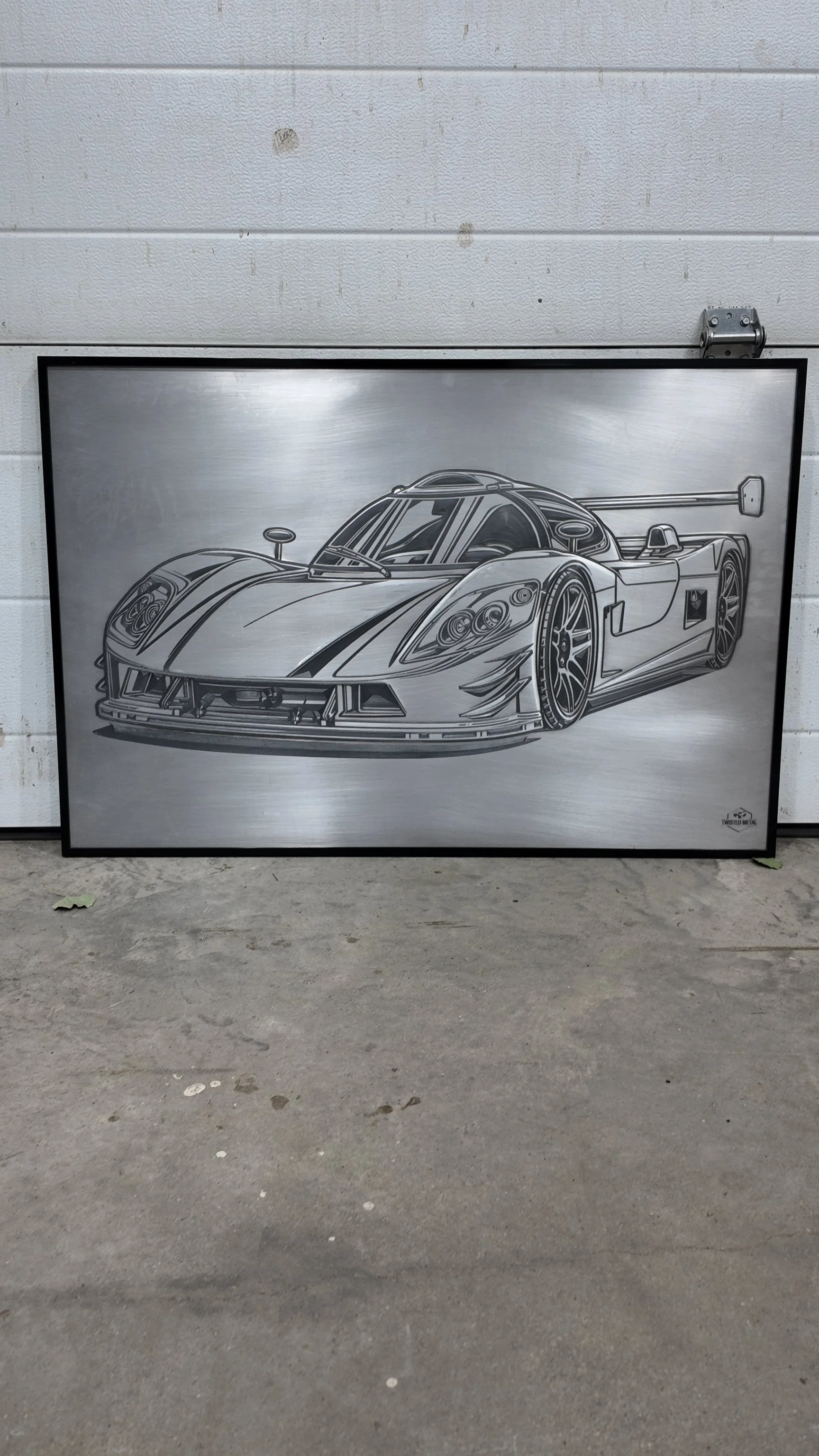 Metal art depicting a race car, mounted and leaning against a white wall.