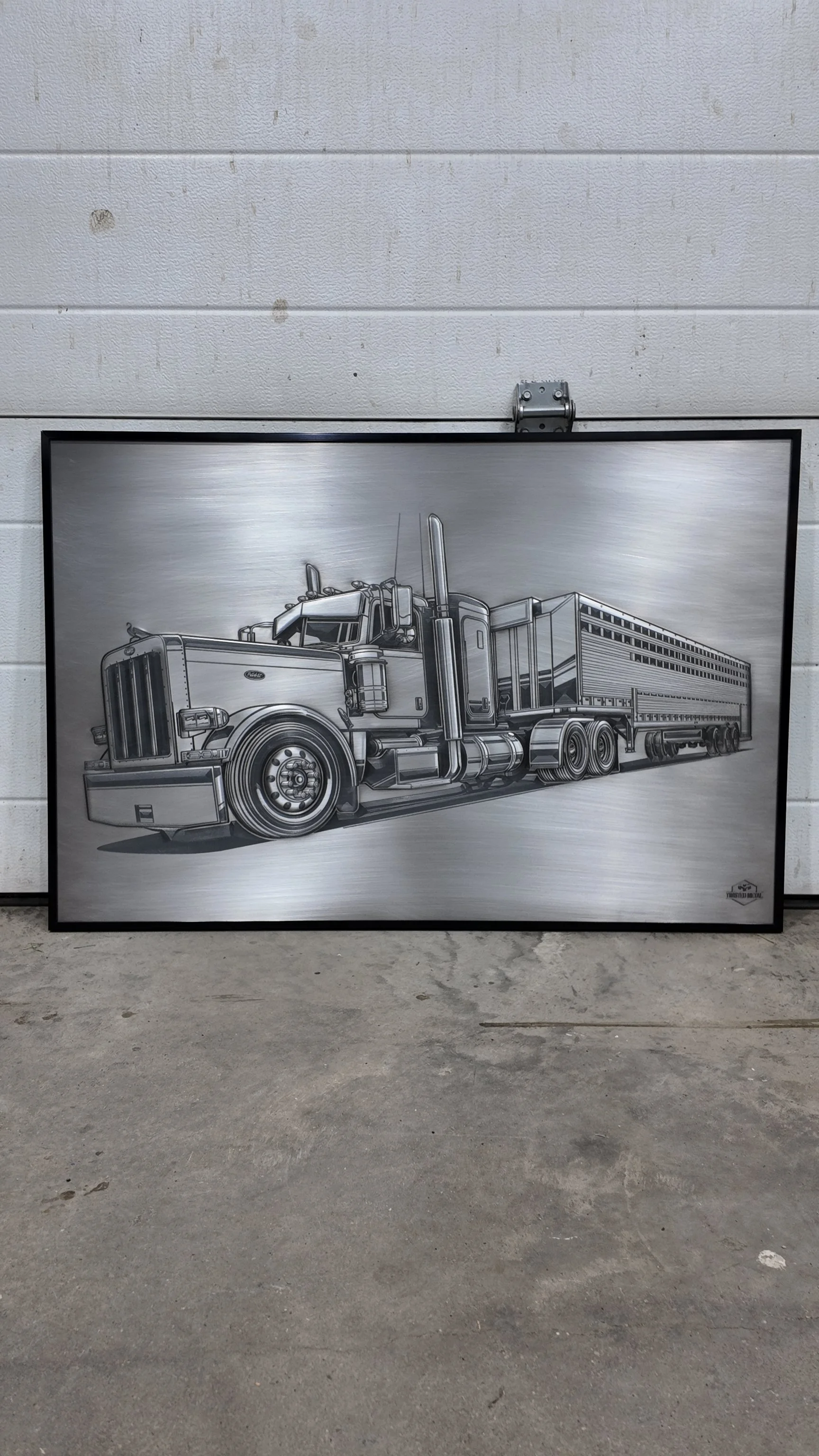 A silver metal artwork of a semi-truck with a trailer, mounted on a wall.