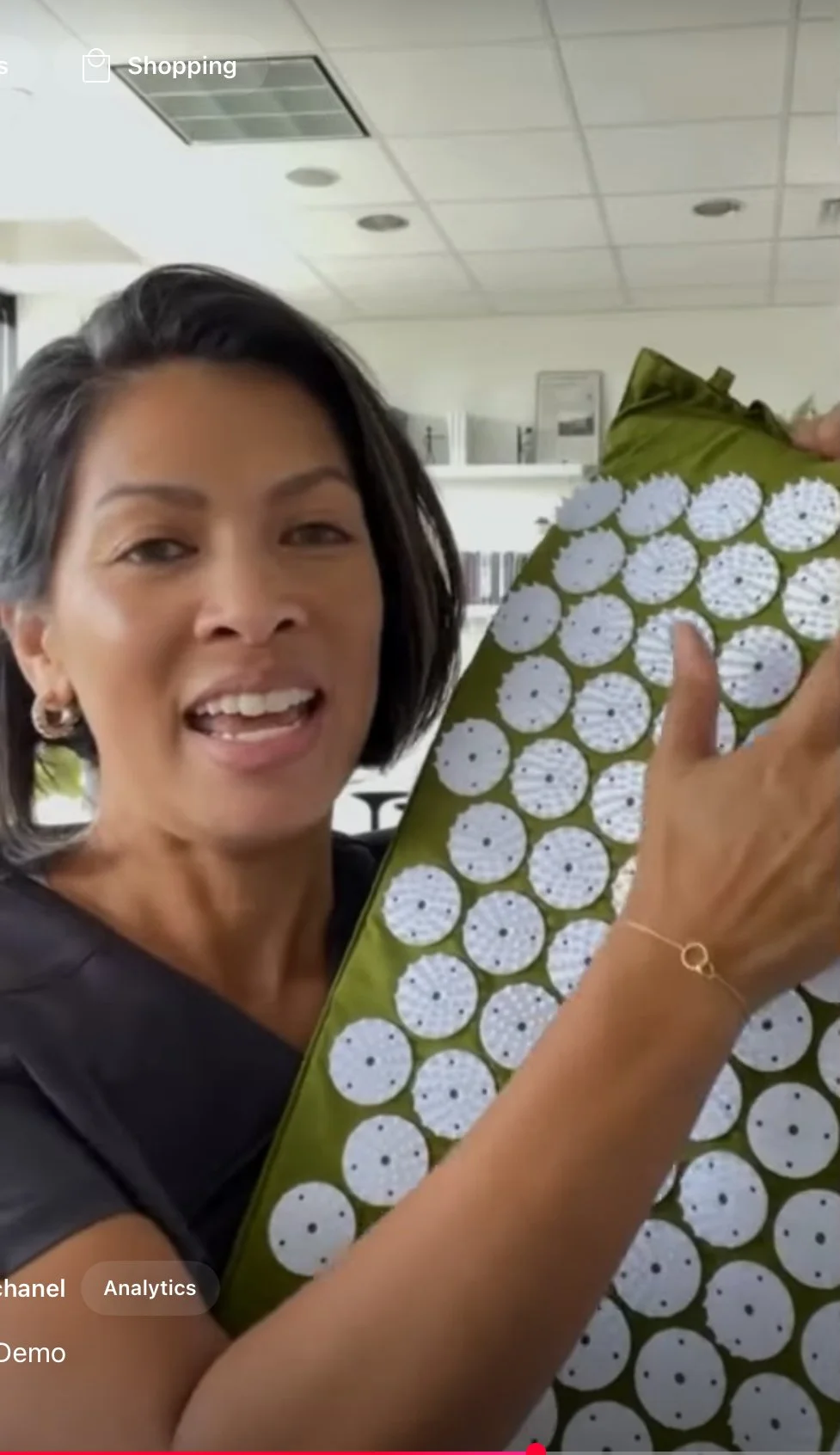 A smiling woman holding a large sheet of round white objects with black dots, possibly batteries or buttons, in an indoor setting.