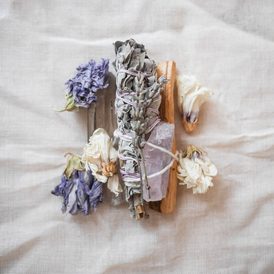 Arrangement of dried flowers, a wooden stick, lavender, a peach-colored stone, and white flowers on a light fabric background.