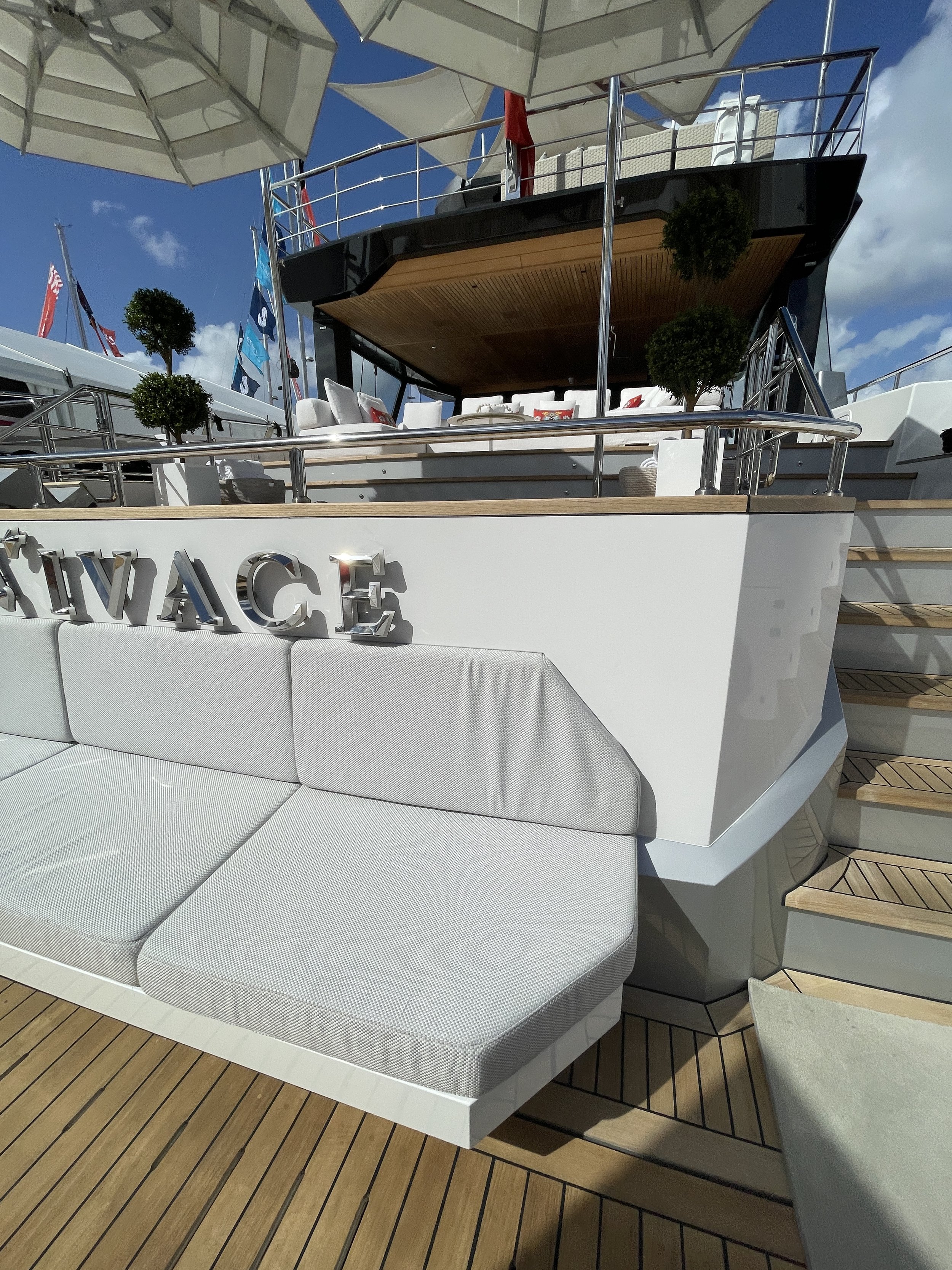 A luxury yacht with white seating, plants, and a shaded upper deck under a clear blue sky.