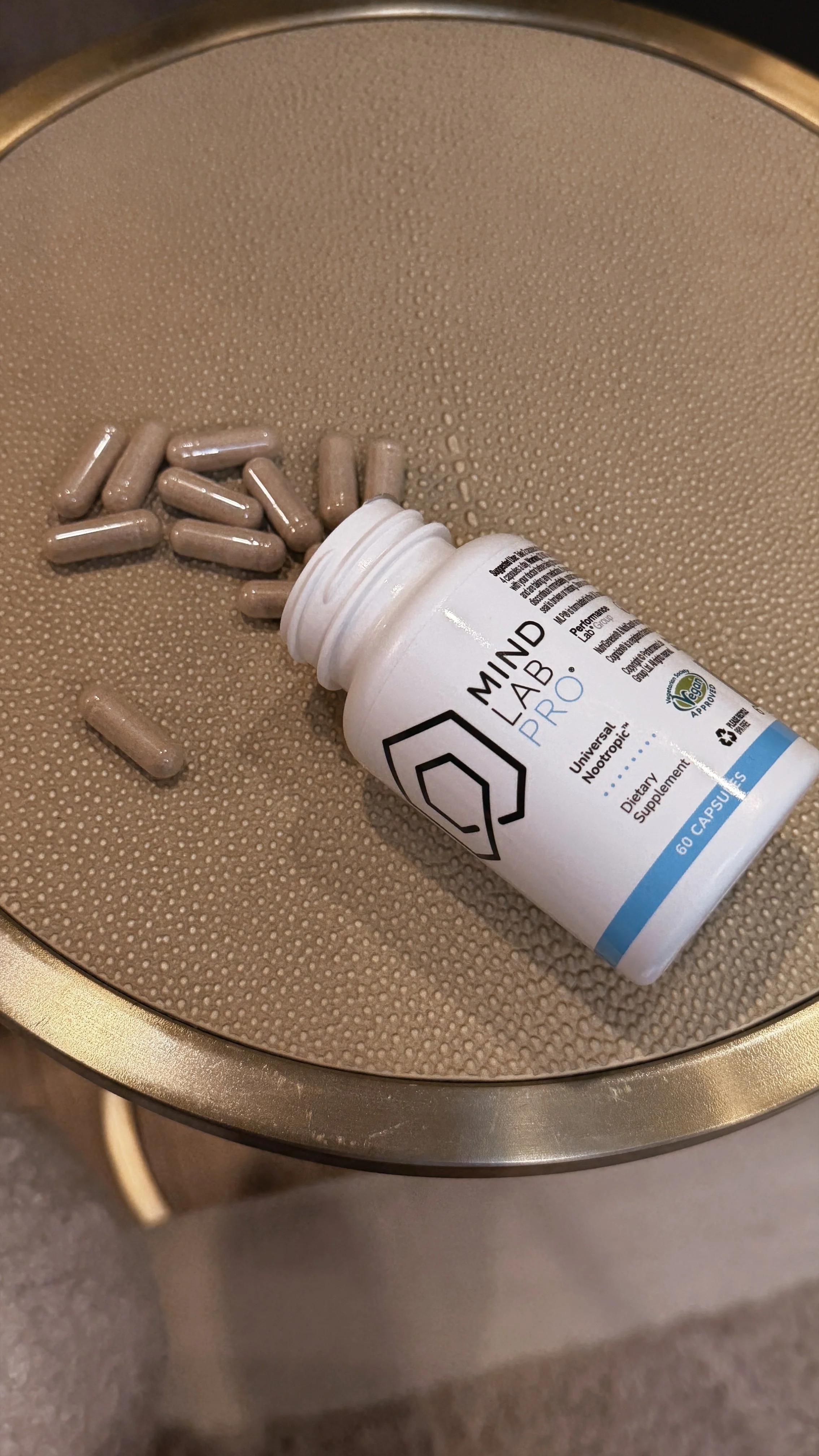 A white bottle labeled 'Mind Lab Pro' with beige capsules spilled next to it, placed on a textured beige surface.