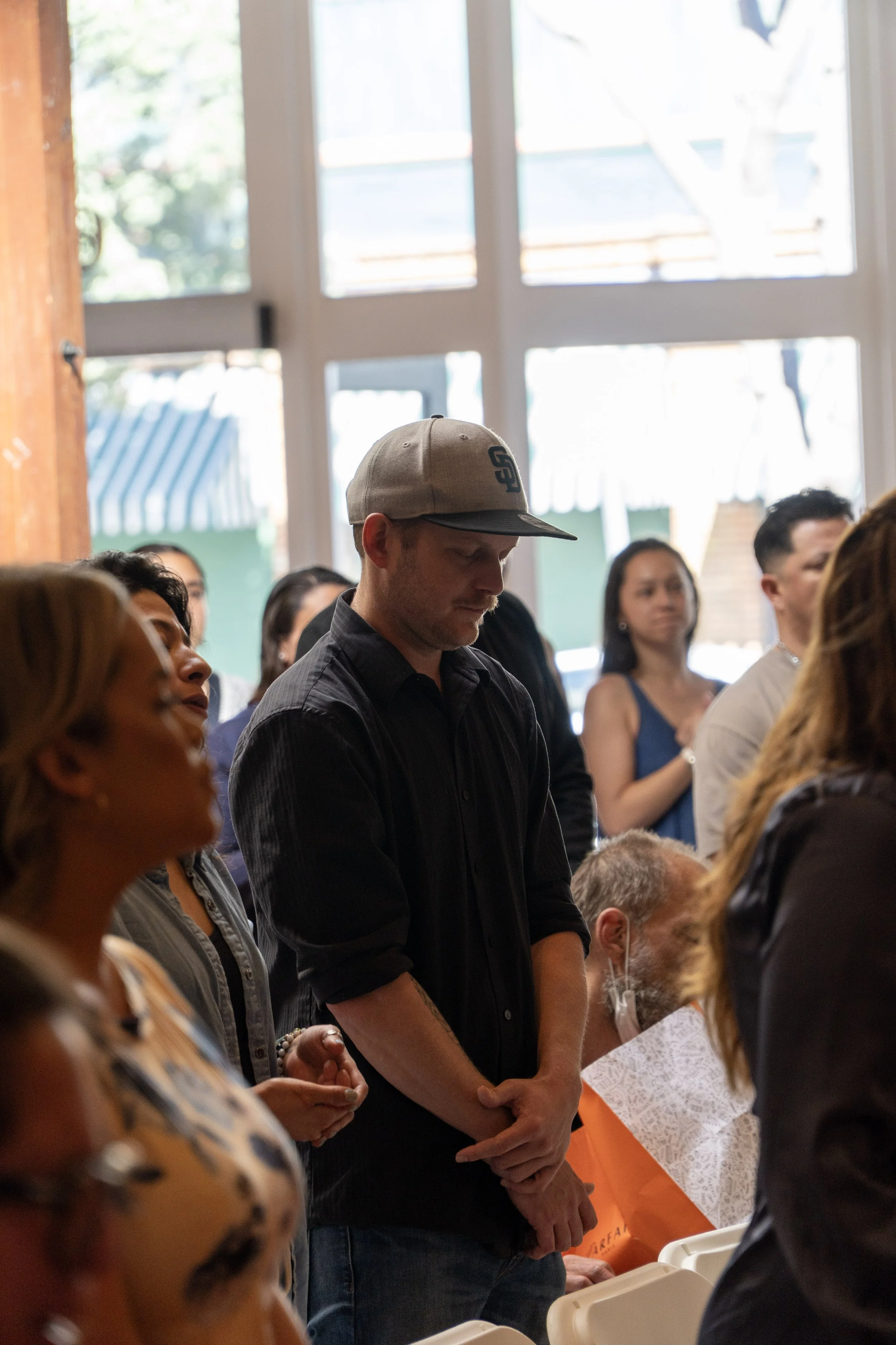 People gathered indoors, some with eyes closed or praying, during a prayer or worship event.