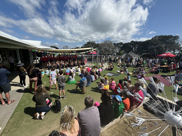 Outdoor event with a crowd watching a performance on a stage under a partly cloudy sky.
