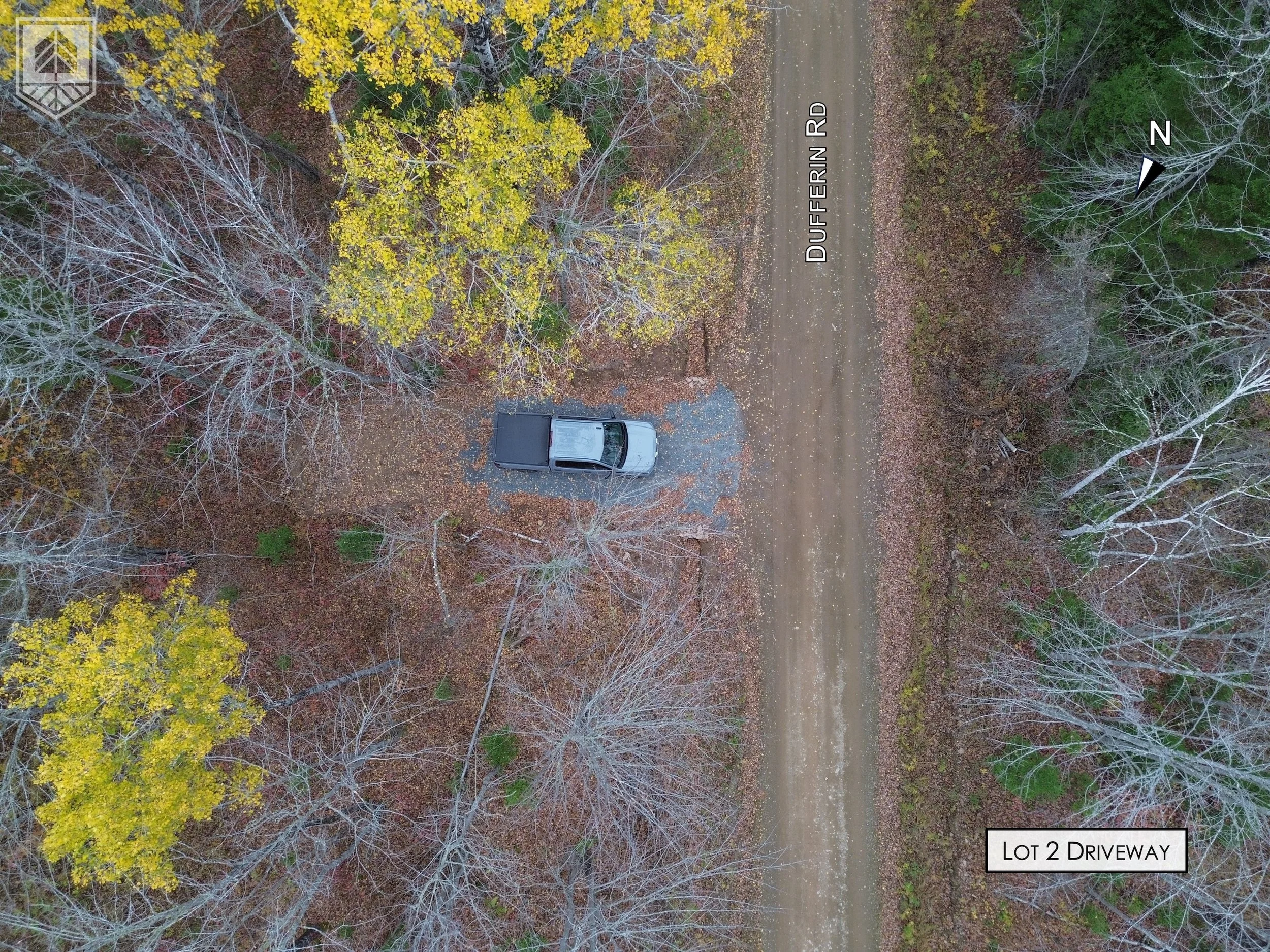 An aerial view of a dirt driveway labeled 'LOT 2 DRIVEWAY' leading to a parked vehicle at the center of the image, surrounded by sparse trees with yellow and brown leaves on a fall day, on Dufferin Road.