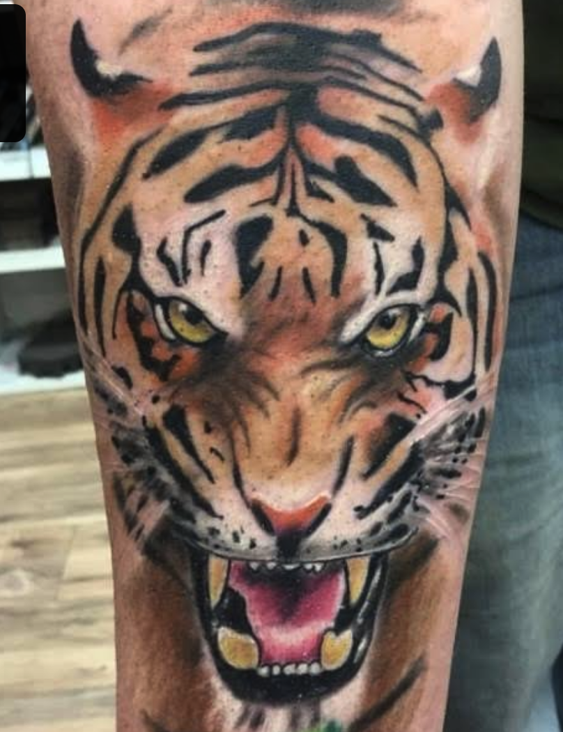 Close-up of a tiger tattoo on skin showing a fierce expression with teeth bared and bright yellow eyes.
