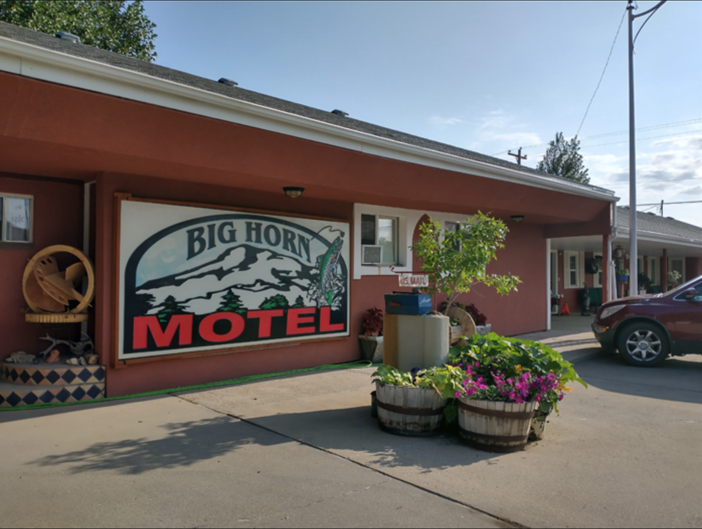 Exterior view of Big Horn Motel with a large sign, potted plants, a parked car, and a covered walkway.