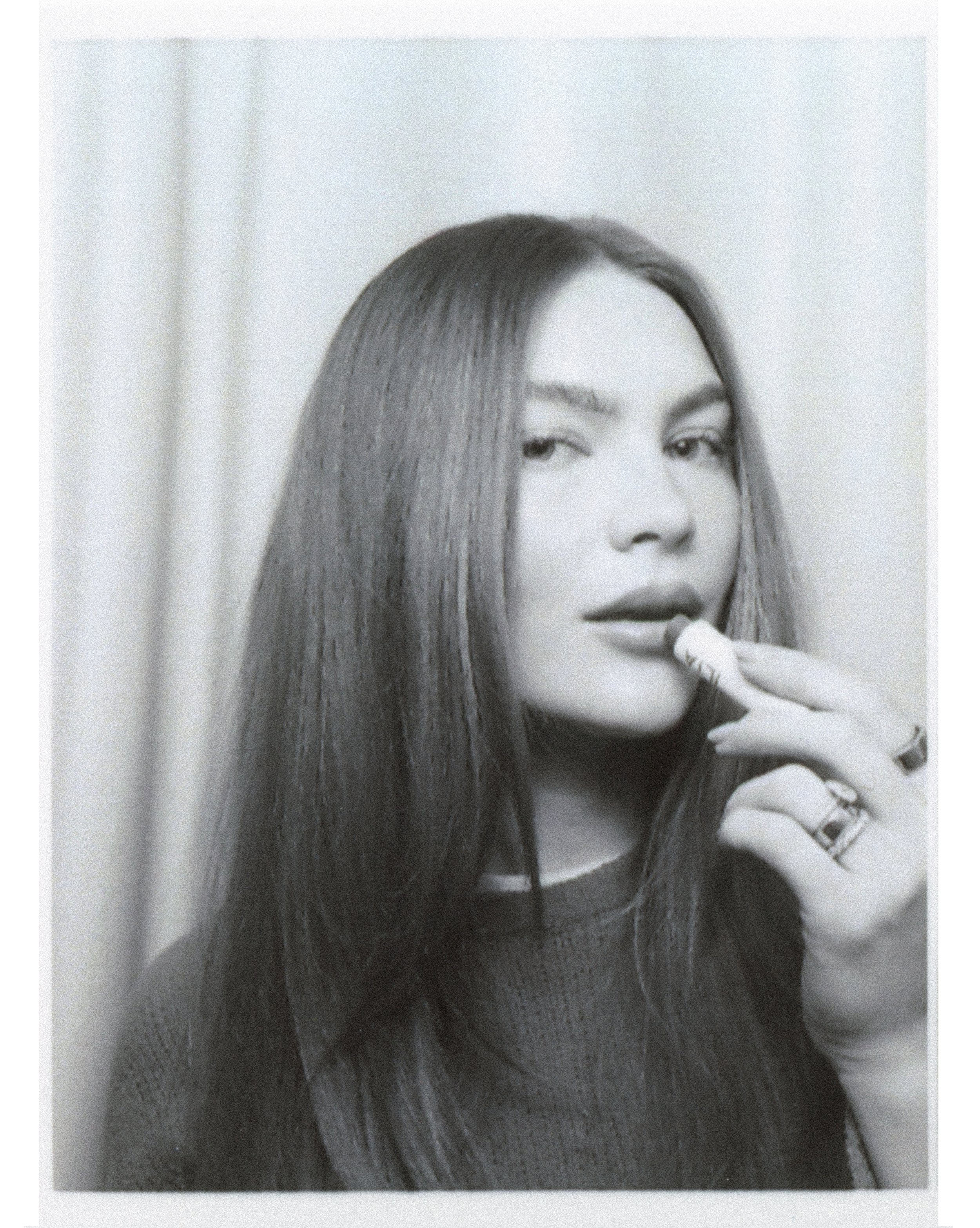 Black and white portrait of a woman with long hair holding a lip balm near her lips.
