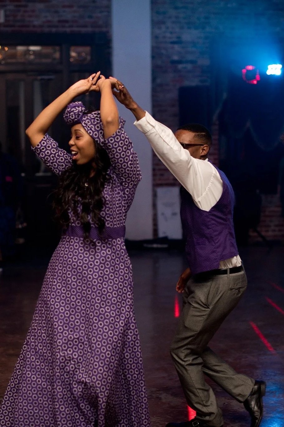 A woman and a man dancing together at an indoor event with guests watching and smiling in the background.