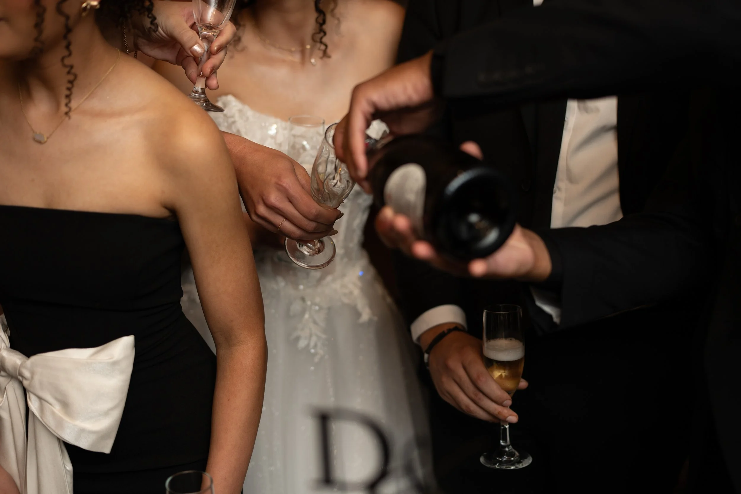 Wedding photography of people at a wedding reception clinking champagne glasses, with a woman in a white dress and a man in a tuxedo holding a champagne bottle in South Louisiana. 