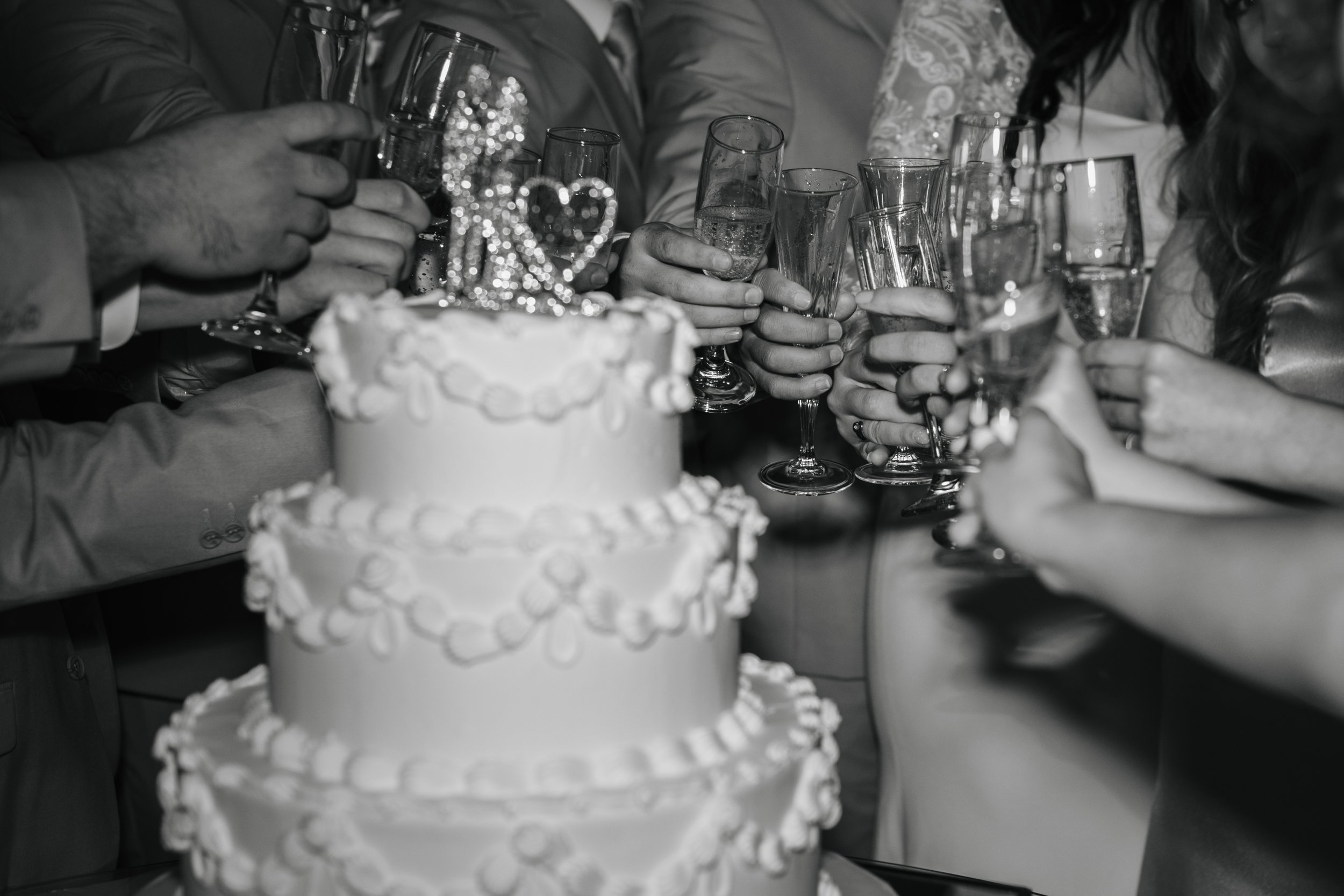 Group of people toasting with champagne glasses in a celebration with a wedding cake in the foreground
