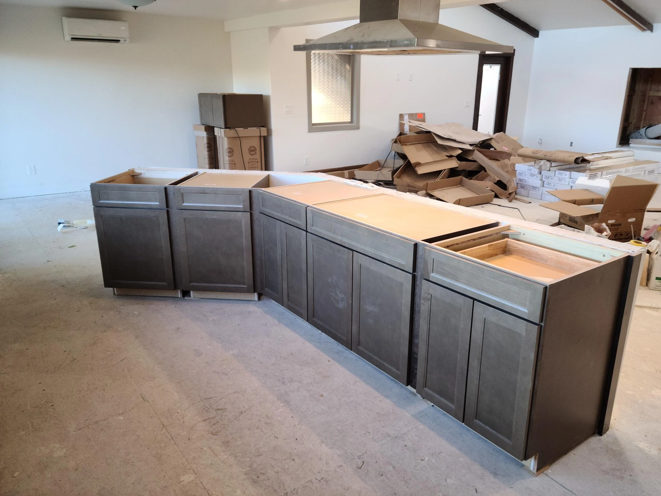 Front view of a house with a porch, stone pillars, and a gabled roof under construction with wood framing visible under the shingles.