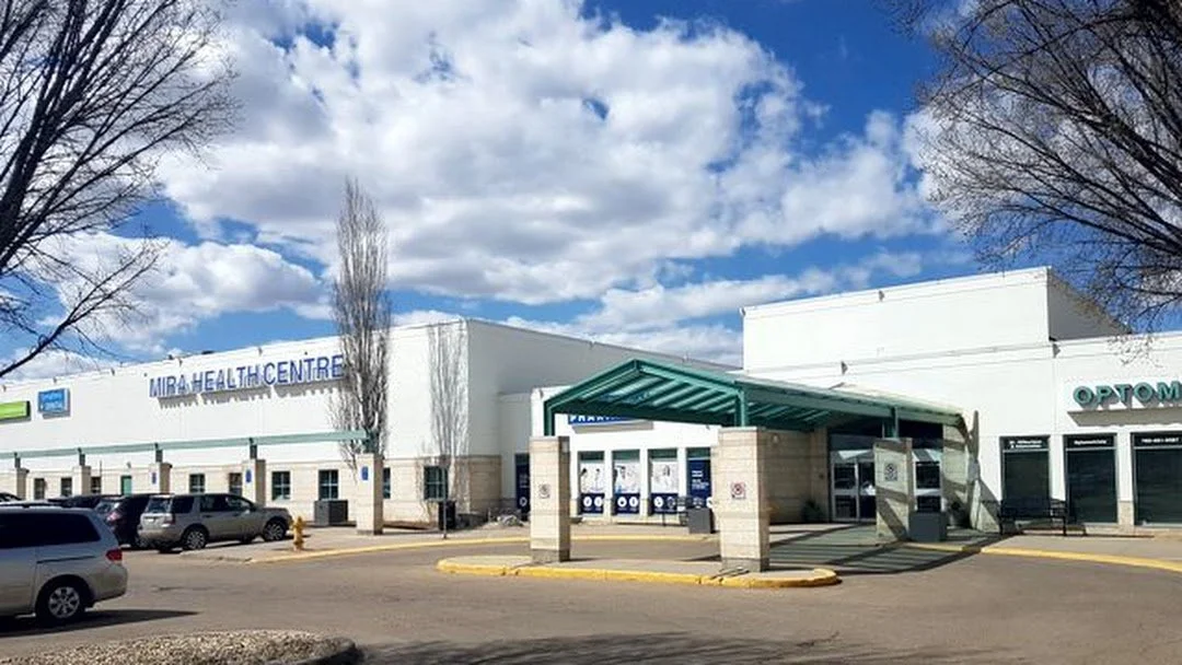 Exterior view of Mira Health Centre with a parking lot in the foreground and a partly cloudy sky.