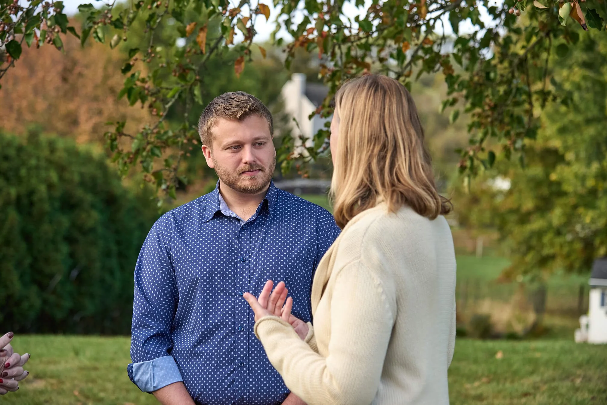 Chris talking to a person outdoors in a park or garden area surrounded by trees and greenery.