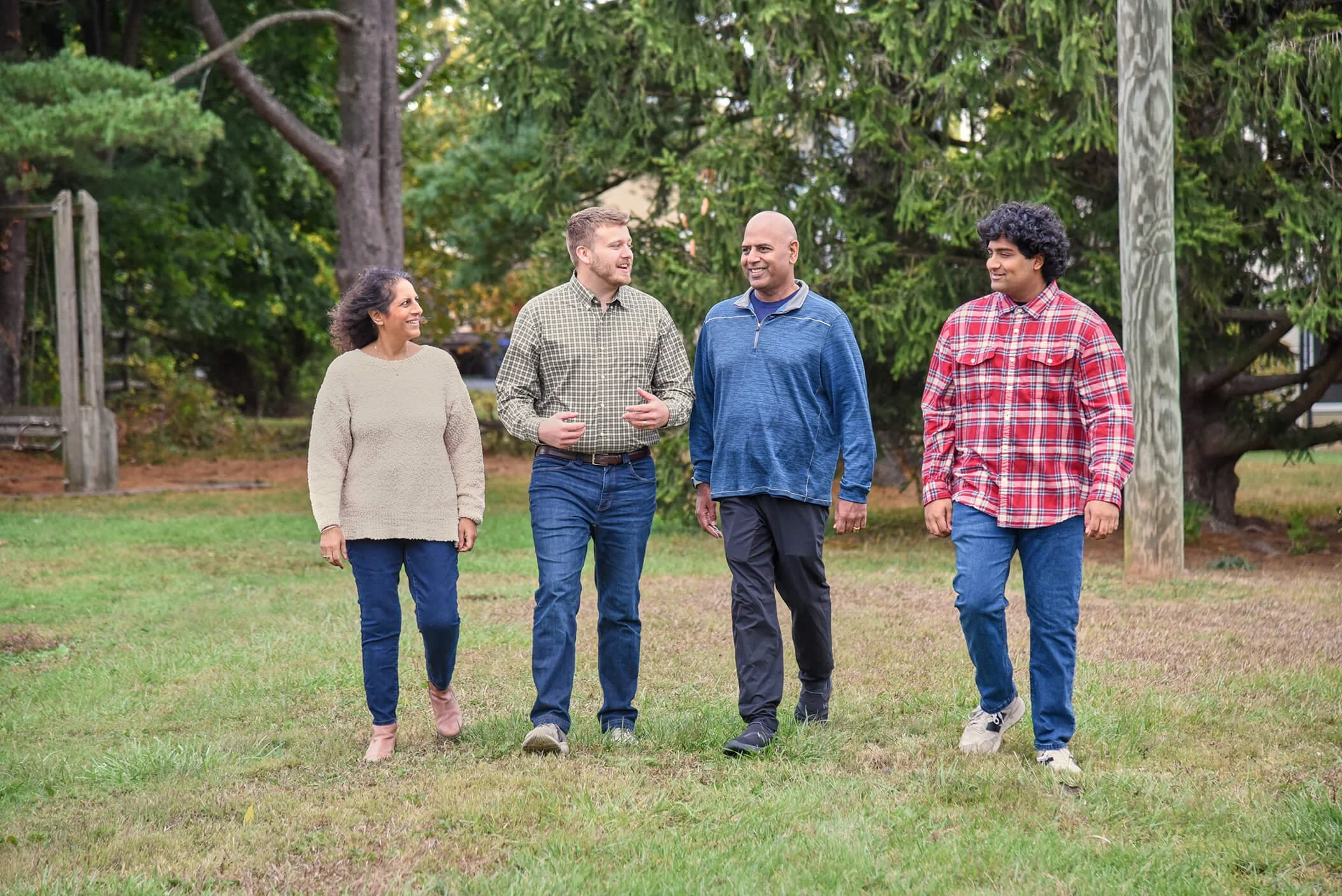 Chris with people walking and talking outdoors on a grassy area with trees in the background