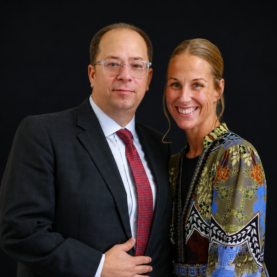 Pastor Brocc Chavis. United The Pentecostal Church of Spring Lake. A man wearing glasses, a gray plaid suit jacket, a light blue shirt, and a dark tie, standing against a black background.