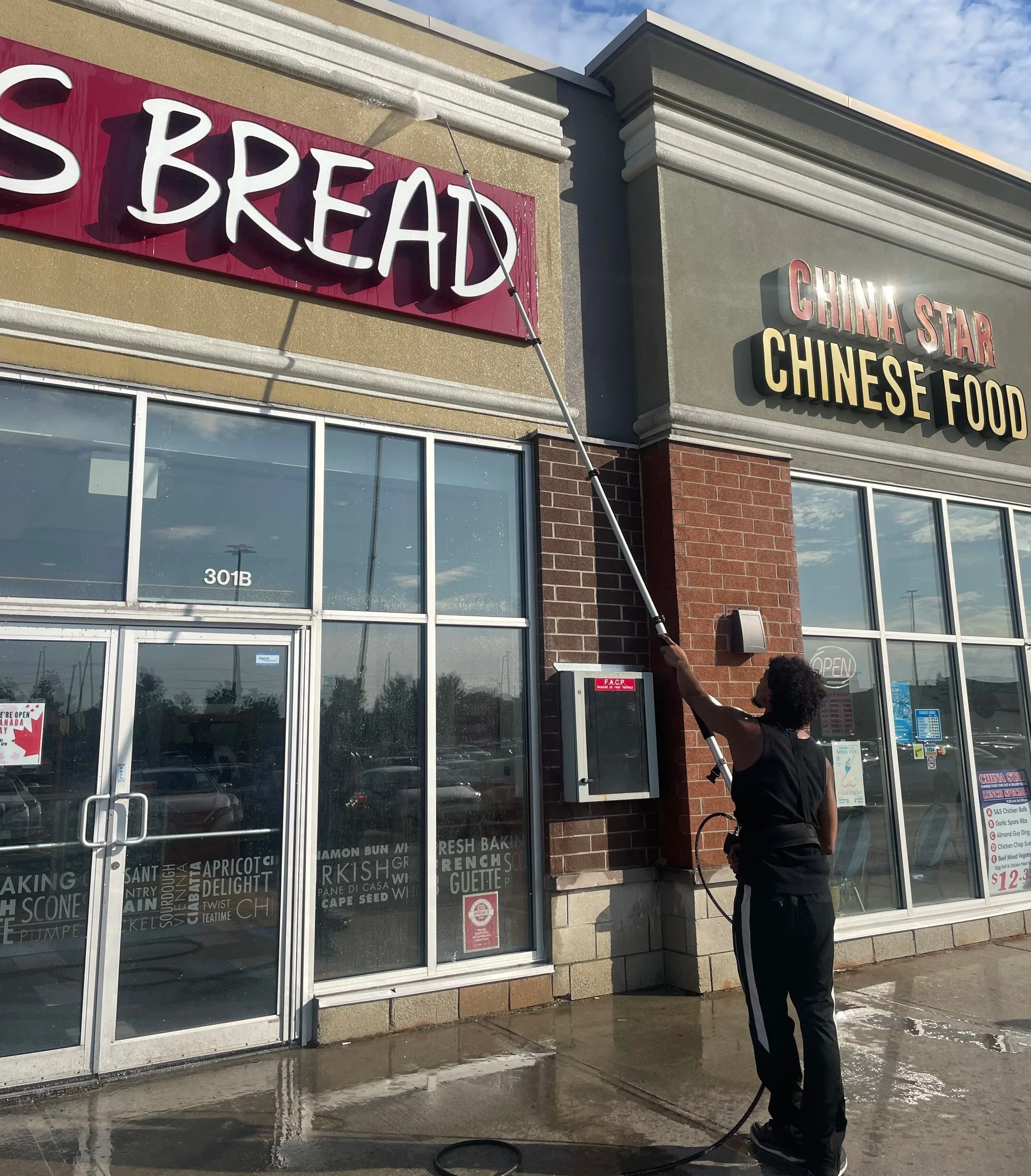 Person cleaning the exterior window of a Chinese restaurant with a long brush attachment on a pole during daytime.