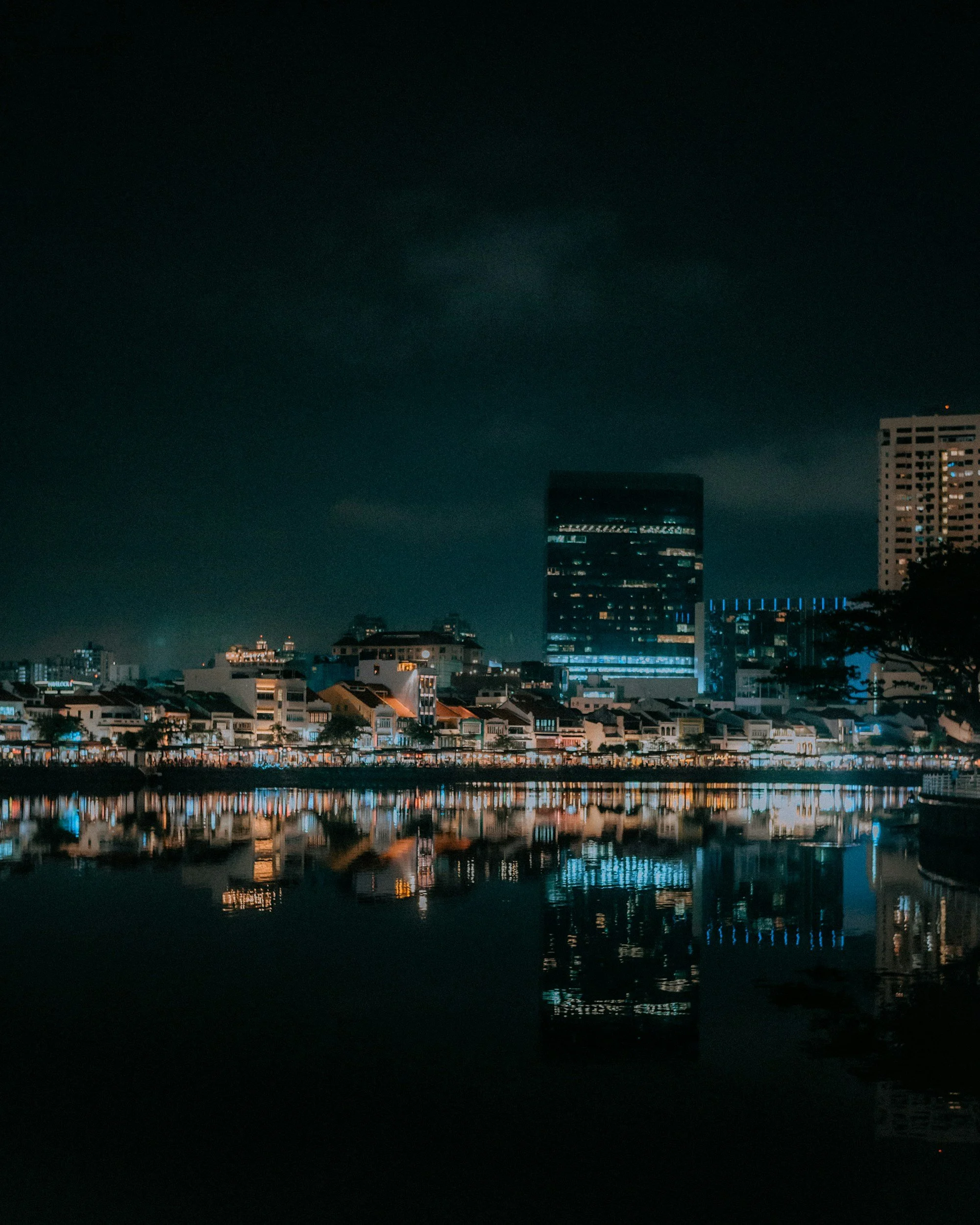 Nighttime cityscape with illuminated buildings and their reflections on a calm body of water.