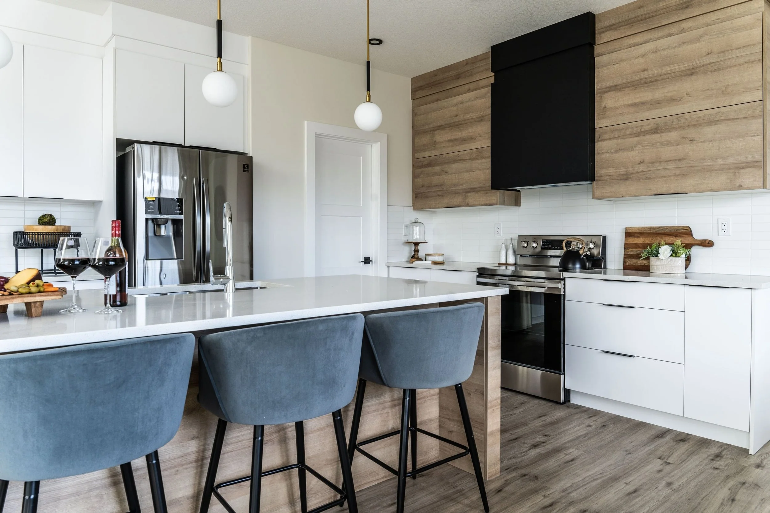 Modern kitchen with white cabinets, stainless steel refrigerator, black stove, wooden accents, and blue bar stools.