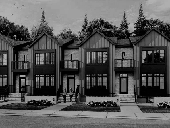 A black and white photograph of modern townhouses with large windows, small front porches, and stairs leading up to doors. Two people are walking on the sidewalk in front of the houses, and there are trees in the background.