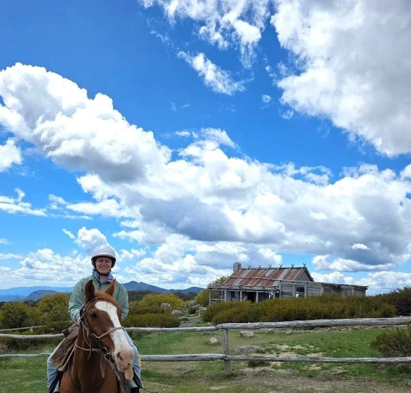 Jojo riding chestnut horse next to timber hut in mountains of Australia